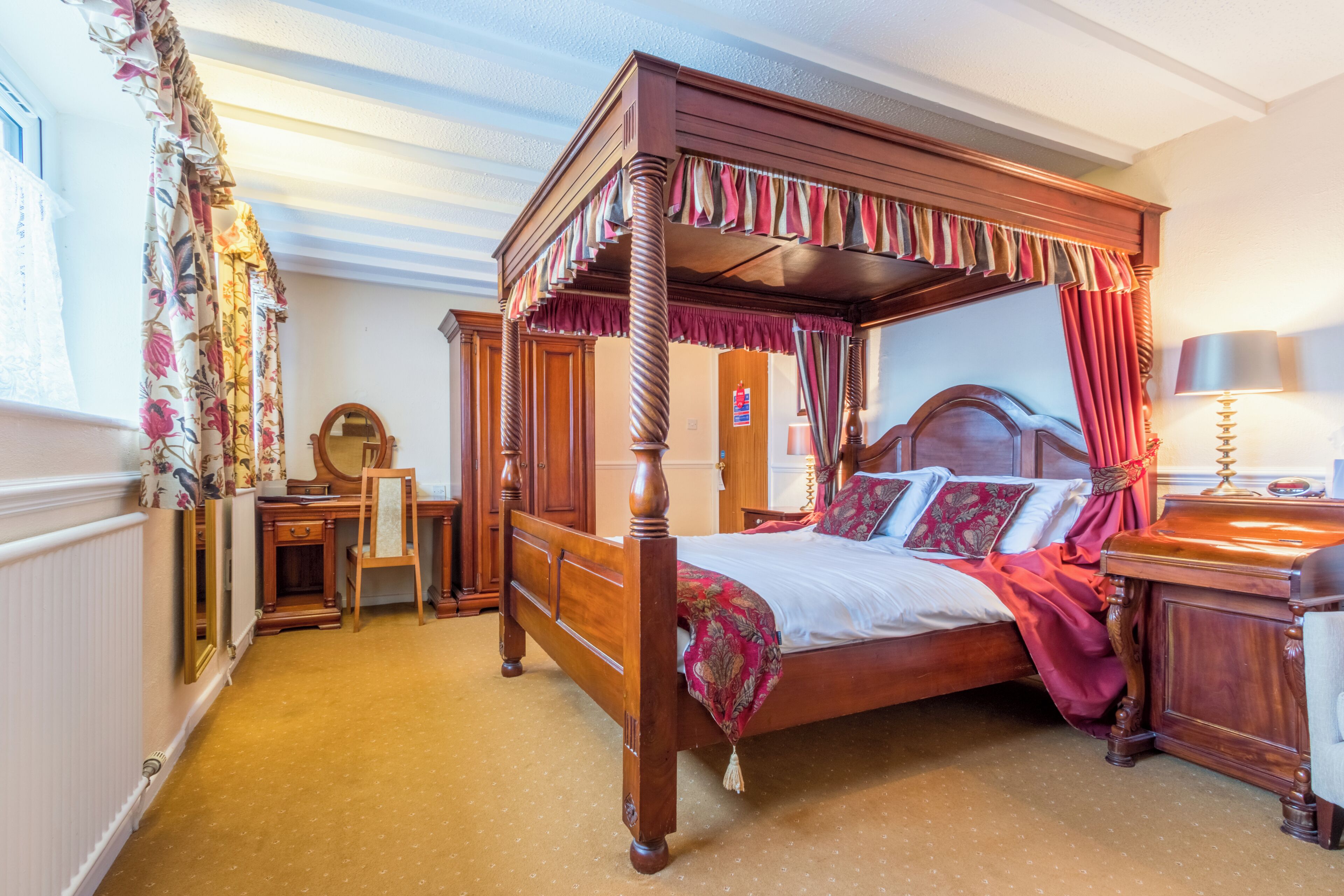 Een hemelbed met baldakijn, een houten bureau, een stoel, een spiegel en een nachtkastje met een lamp.