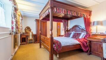 Een hemelbed met baldakijn, een houten bureau, een stoel, een spiegel en een nachtkastje met een lamp.
