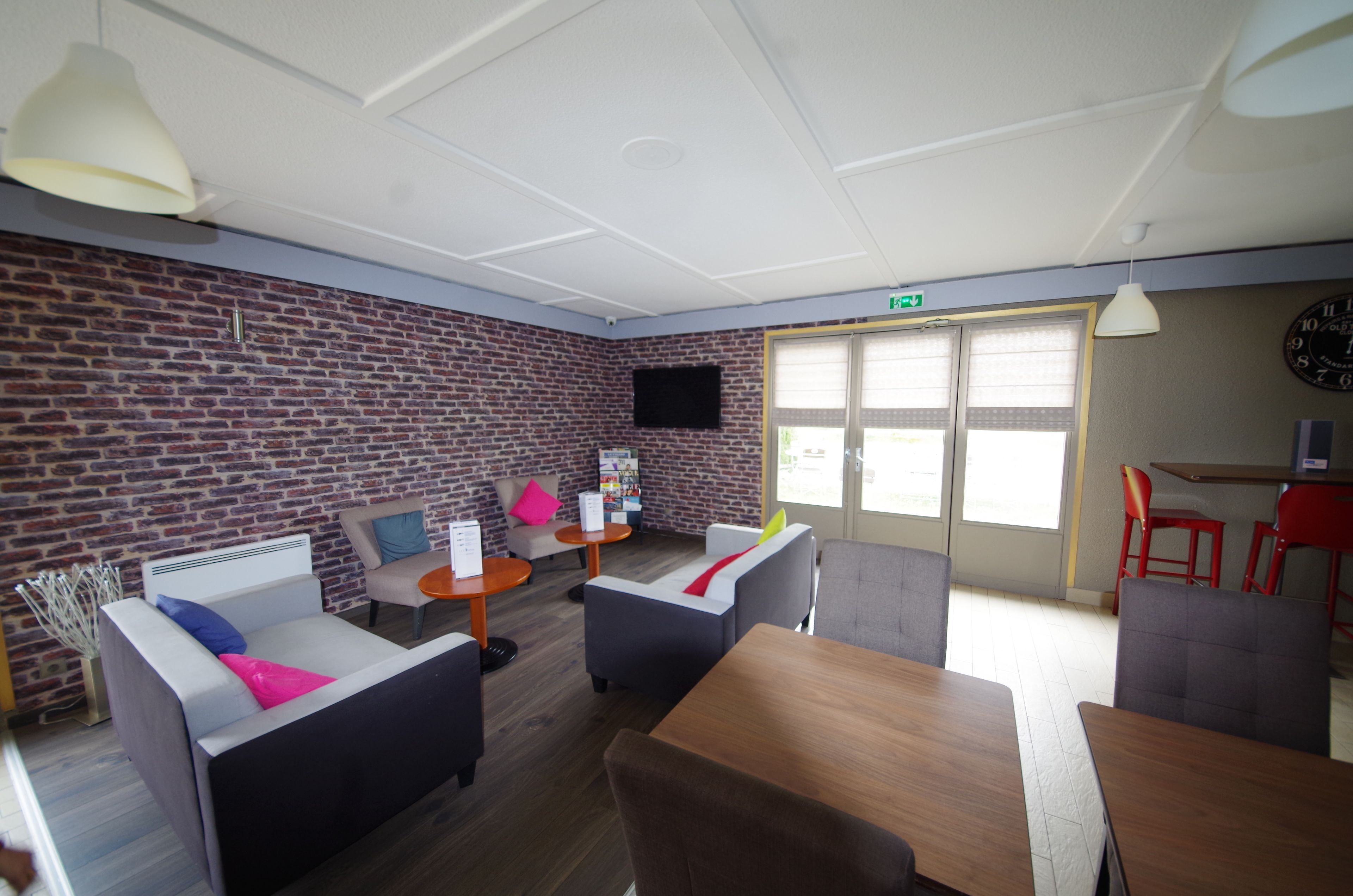 A modern lounge area with brick walls, comfortable seating, a flat-screen TV, and a wooden table.