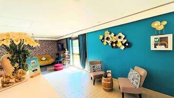 A modern living room with a brick wall, teal accent wall, and wooden flooring. There are two sofas, a coffee table, and a decorative vase with flowers.