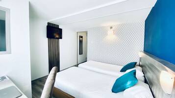 A hotel room with a bed, a desk, a TV, and a patterned wall.