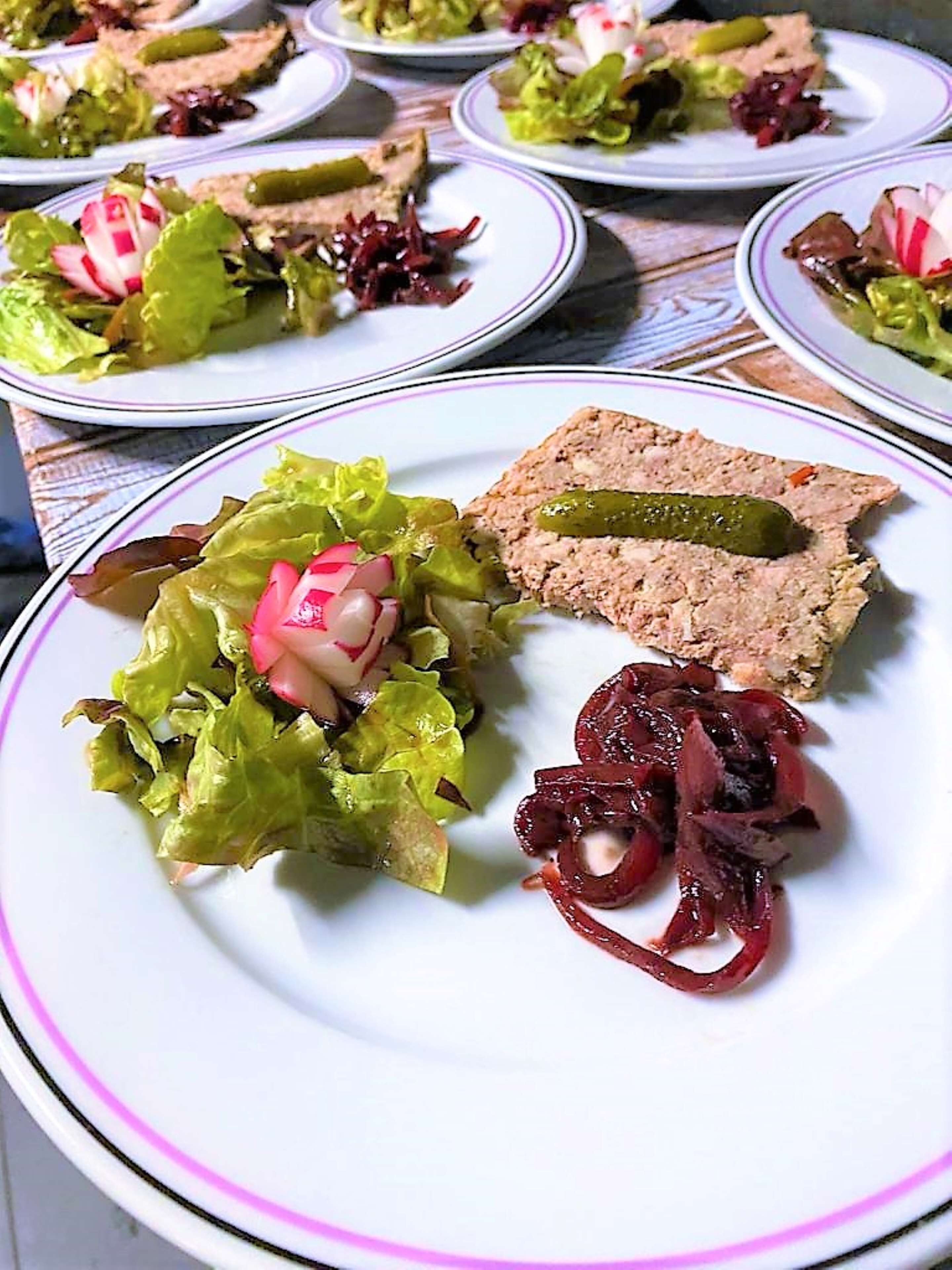Una mesa con platos de comida, incluyendo una ensalada con rábanos y un guiso de carne con un pepinillo.