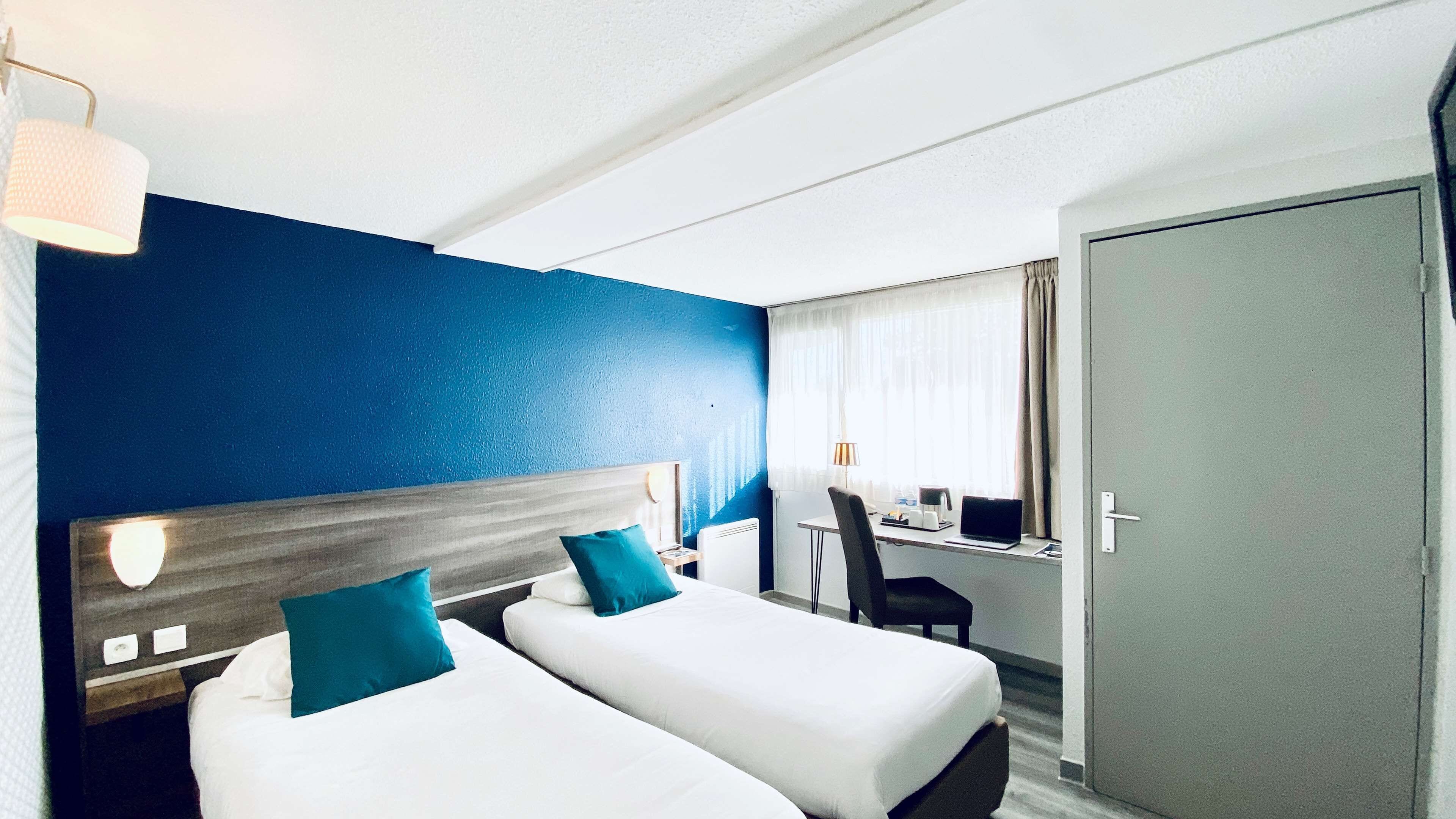 Una habitación de hotel con dos camas, un escritorio, una silla y una puerta.