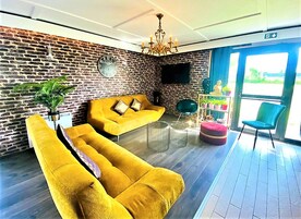 Una sala de estar moderna con pared de ladrillo, sofás amarillos, una araña y vista al exterior.
