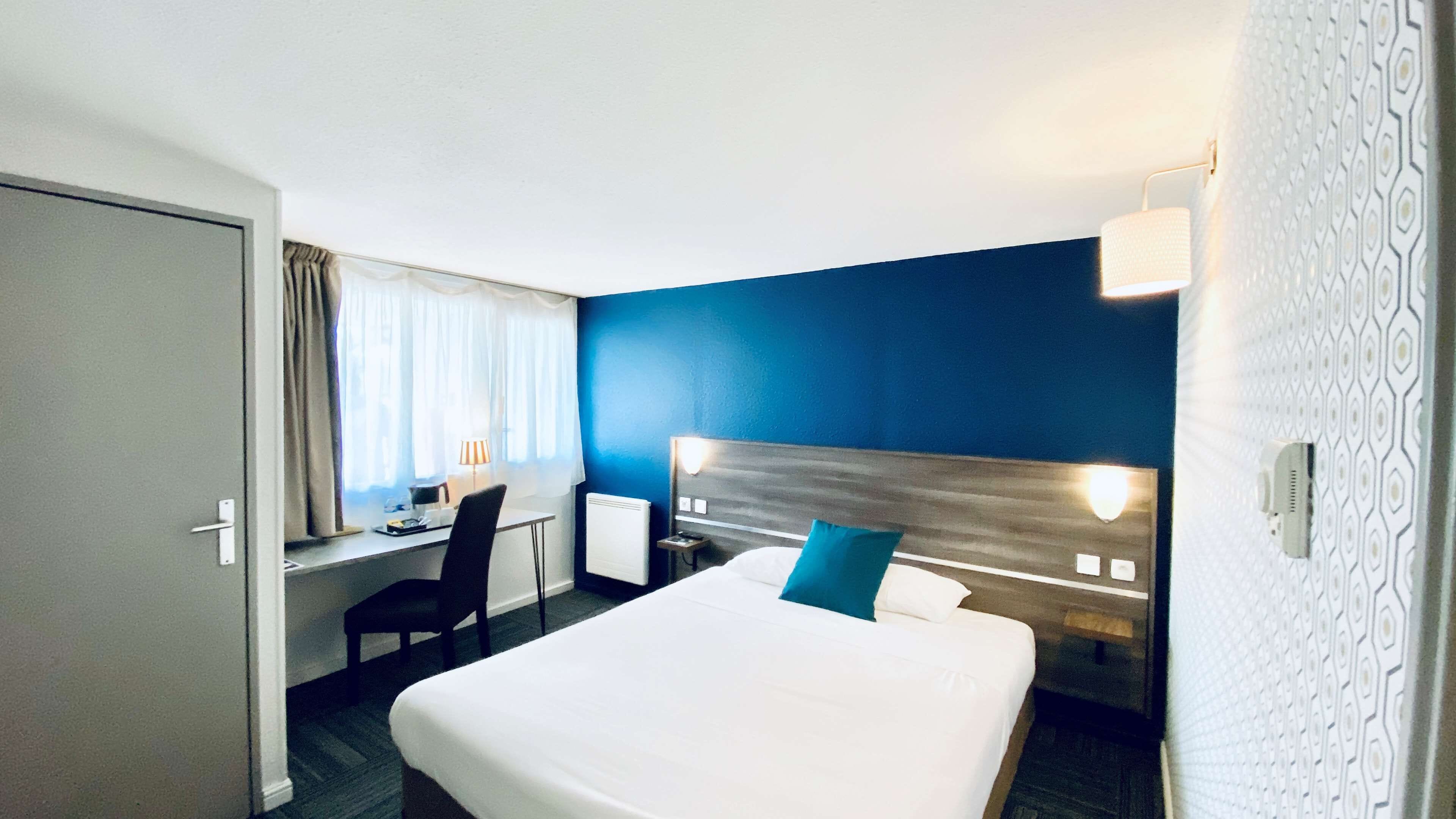 Una habitación de hotel con una cama grande, un escritorio con una silla, una mesita de noche y una mesita auxiliar.
