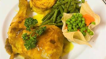 Une assiette contenant un morceau de poulet rôti, des haricots verts, une pomme de terre et une petite portion de petits pois et de carottes.