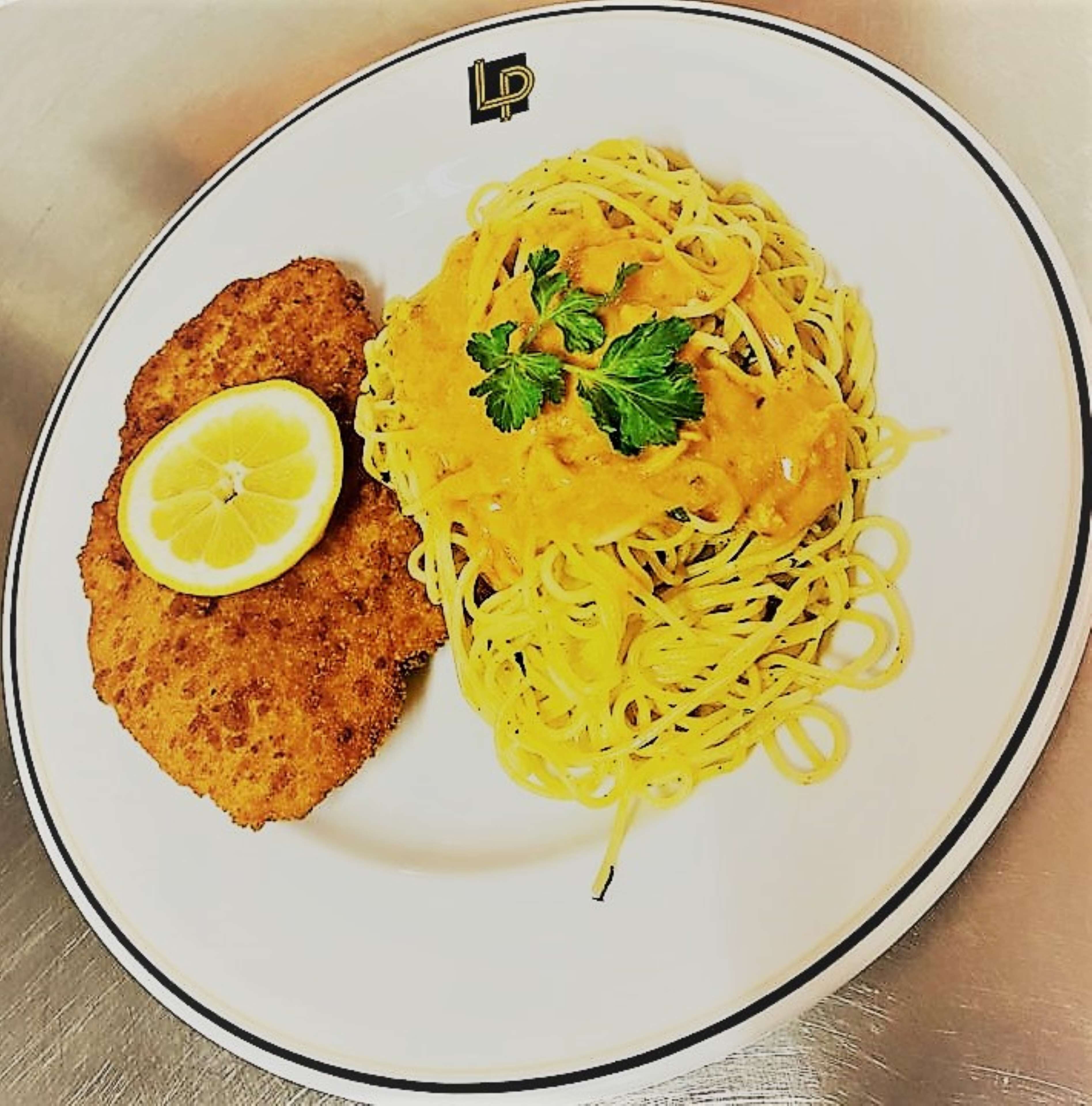 Un plato con milanesa, espagueti y una rodaja de limón.