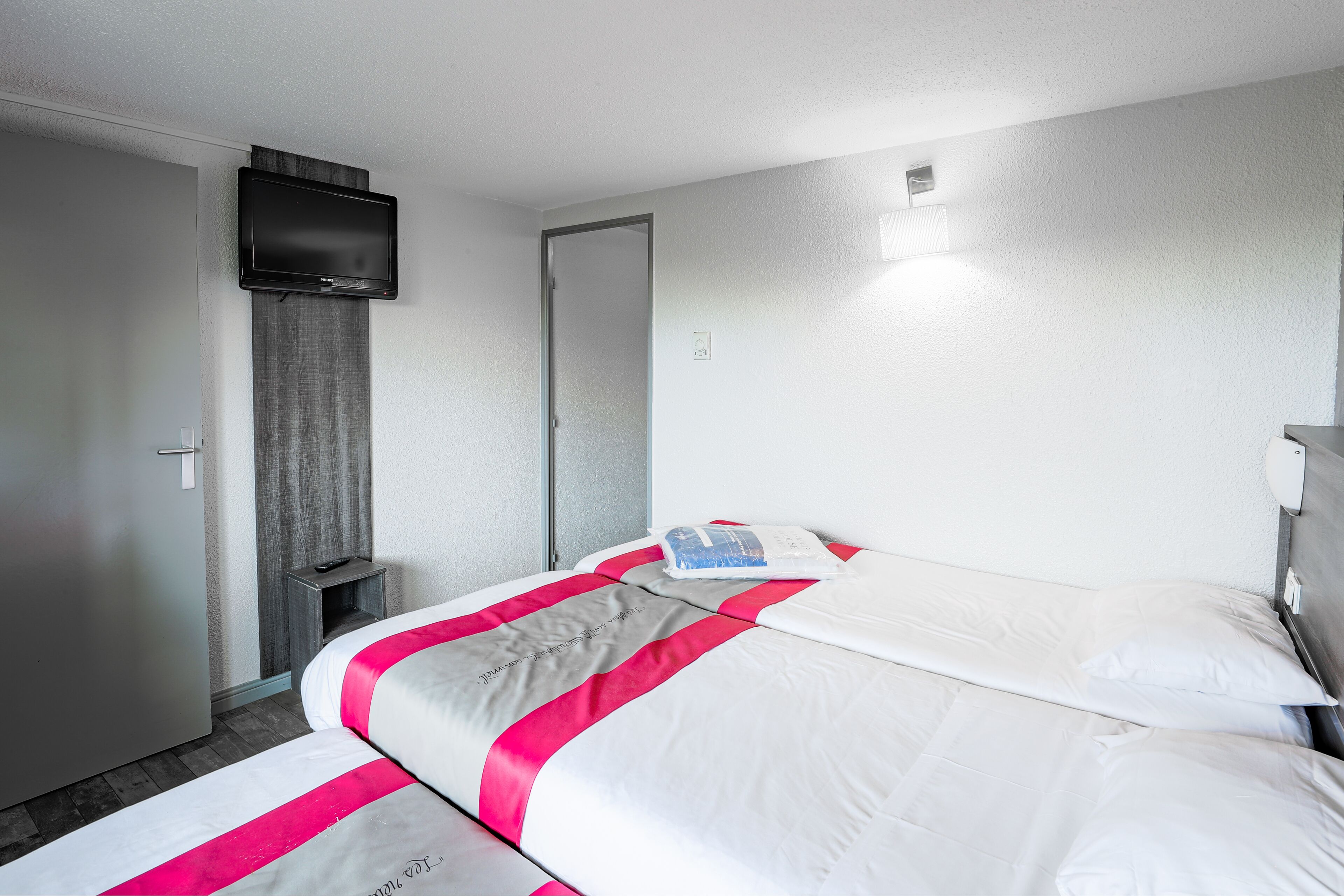 A hotel room with a bed, a TV mounted on the wall, a door, and a small bedside table.