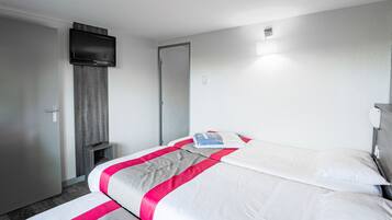 A hotel room with a bed, a TV mounted on the wall, a door, and a small bedside table.
