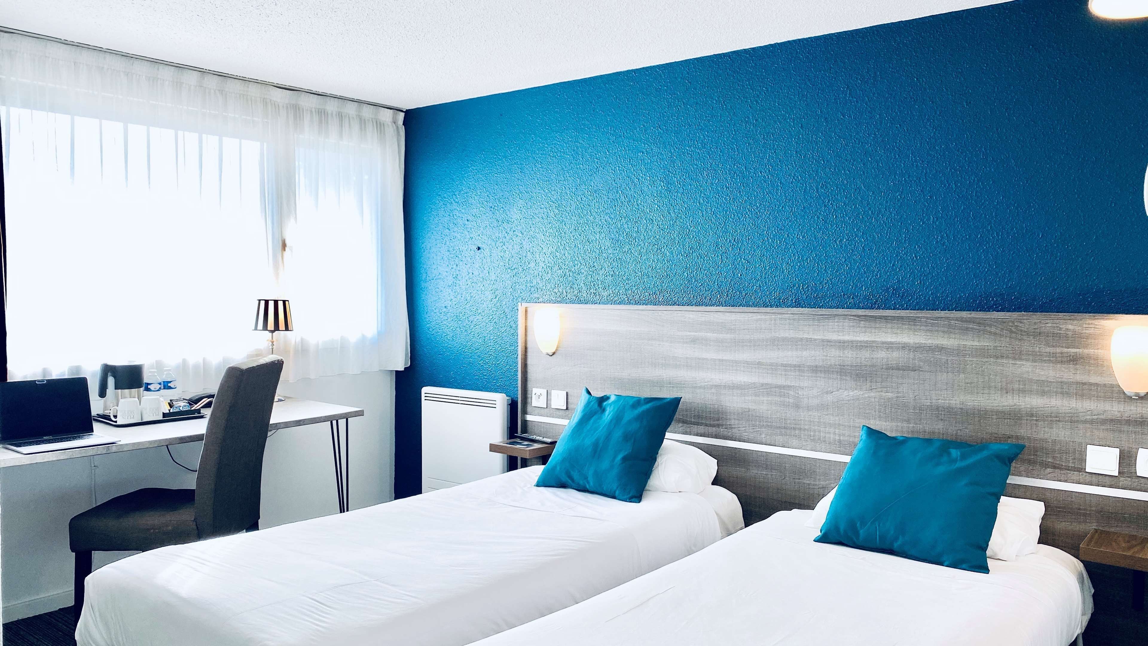 Habitación de hotel con dos camas, un escritorio con una computadora portátil, una silla y una ventana con cortinas.