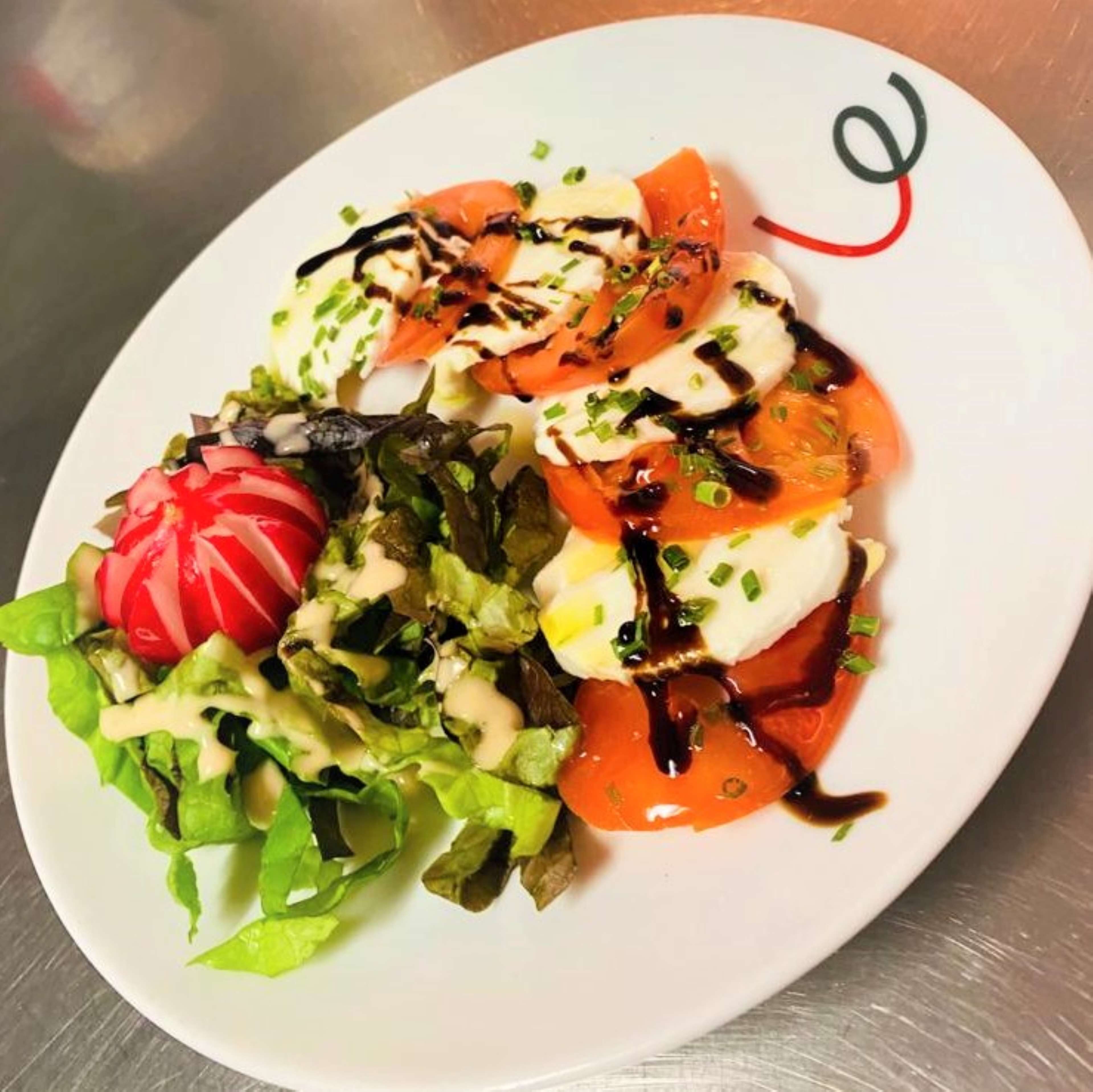 A plate of Caprese salad with tomatoes, mozzarella, and basil, drizzled with olive oil and balsamic vinegar.