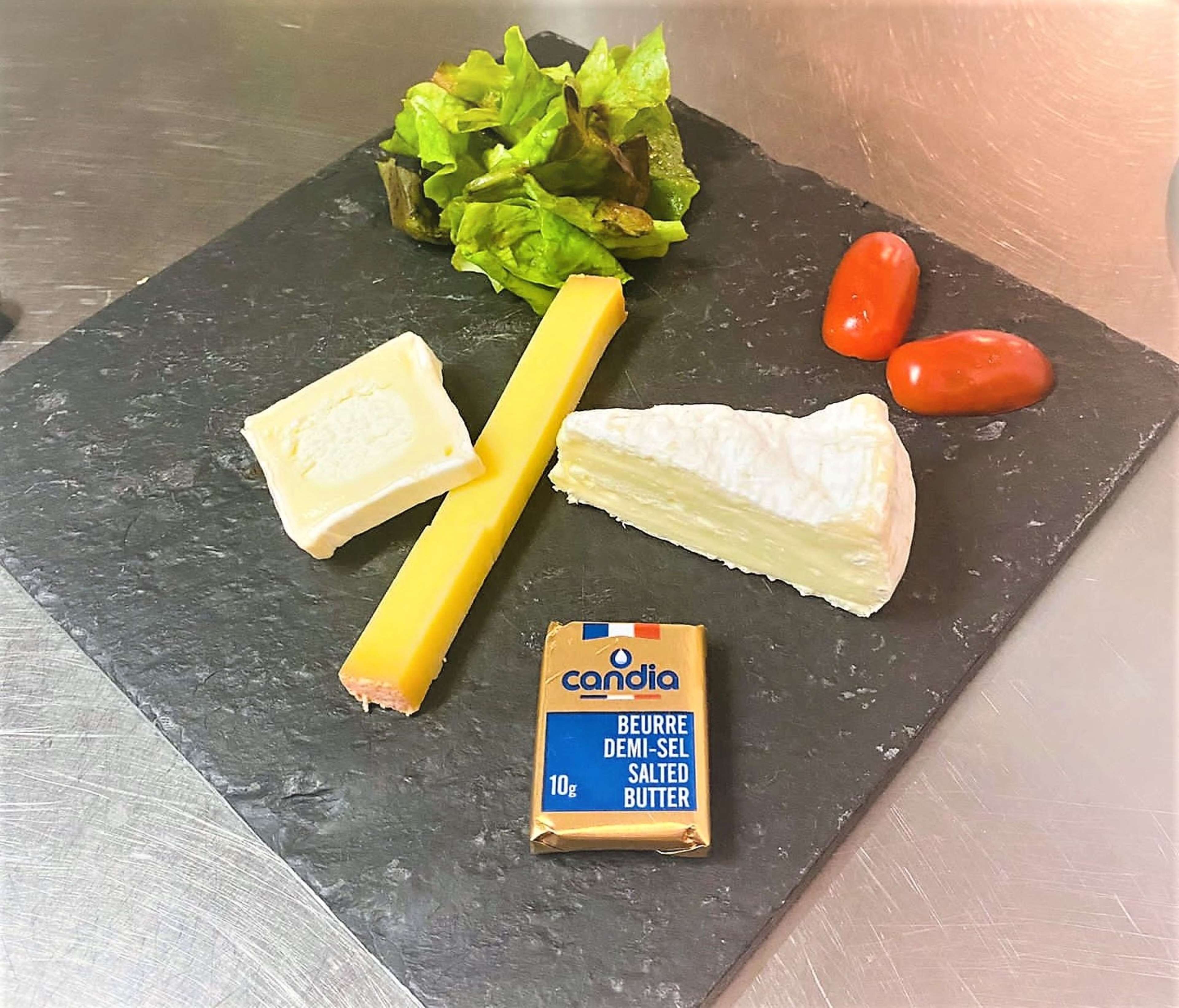 Un plateau de fromages avec différents types de fromages, une portion de beurre et quelques légumes.
