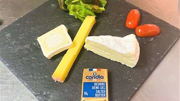 Un plateau de fromages avec différents types de fromages, une portion de beurre et quelques légumes.