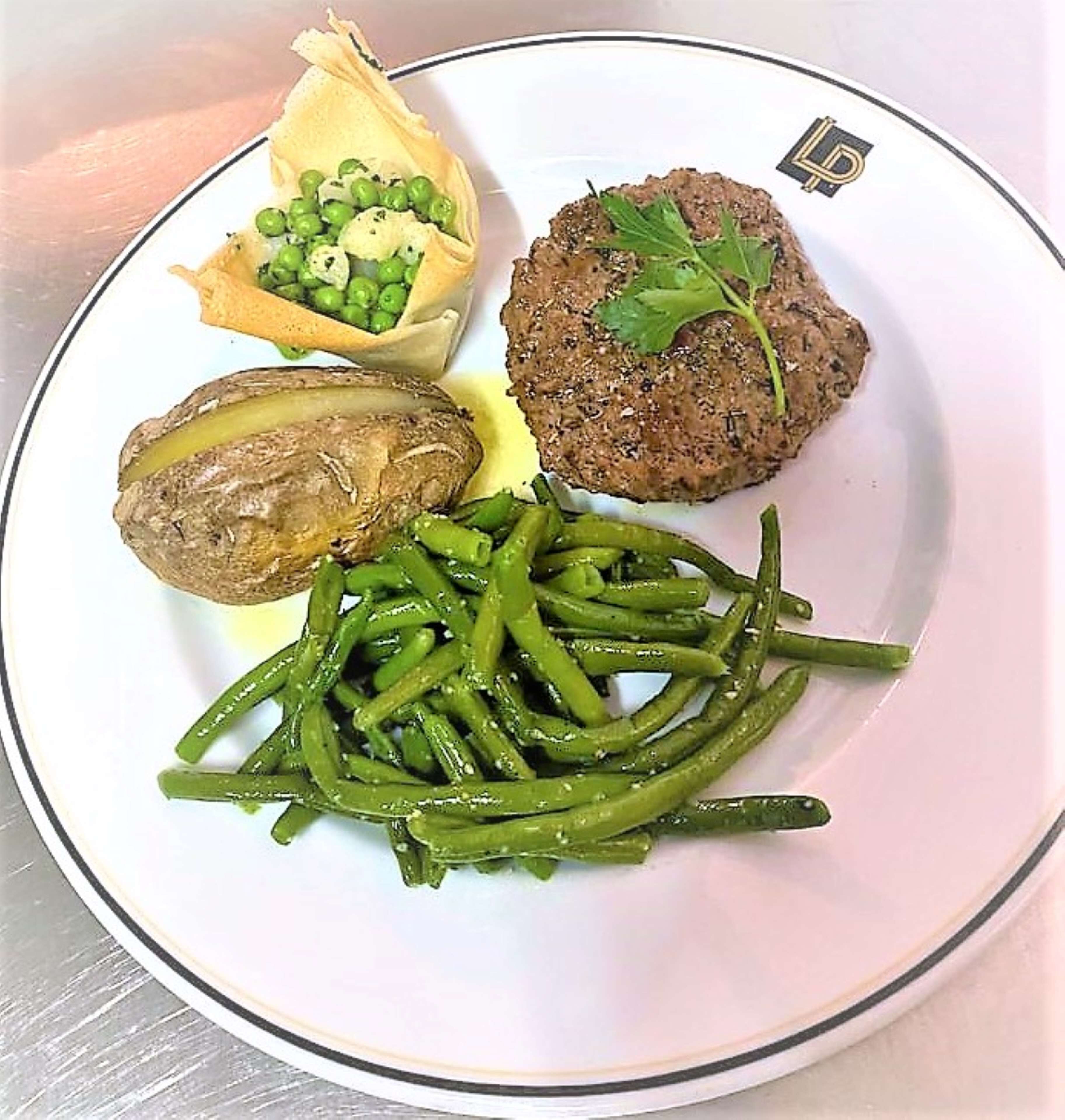A plate with a meat patty, peas, a baked potato, and green beans.