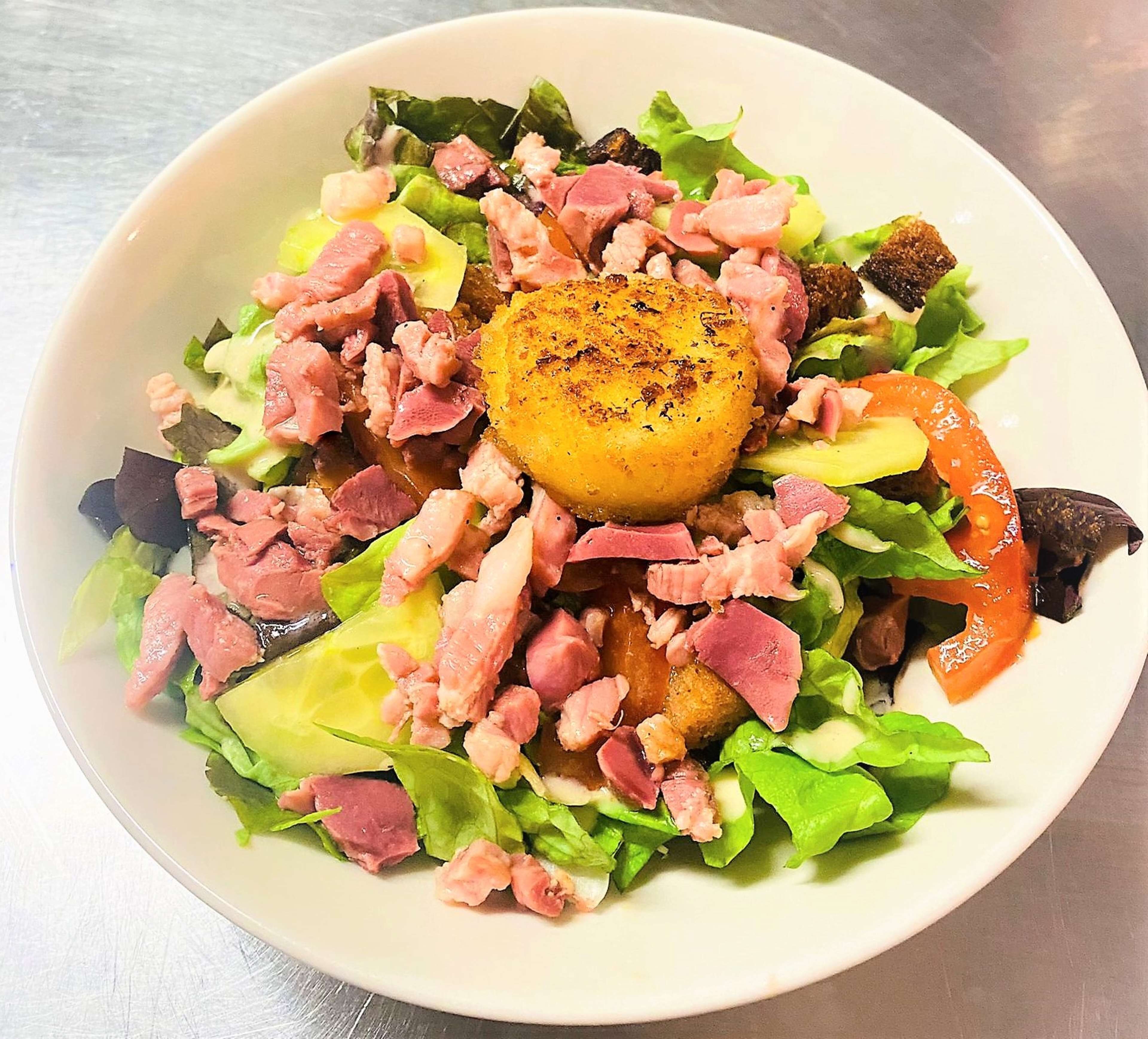 Una ensalada con diversos ingredientes, incluyendo lechuga, tomates y un elemento dorado en el centro.