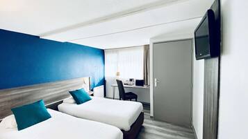 A hotel room with two beds, a desk, a chair, a television, and a door.