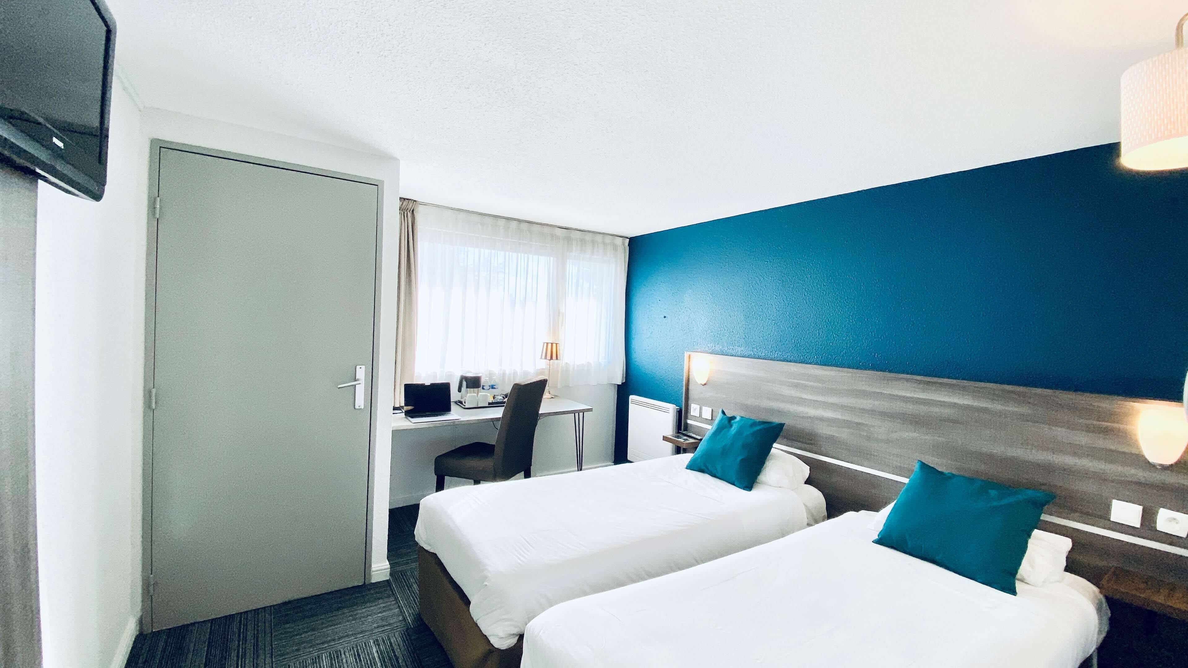 A hotel room with two beds, a desk, a chair, a TV, and a window with curtains.