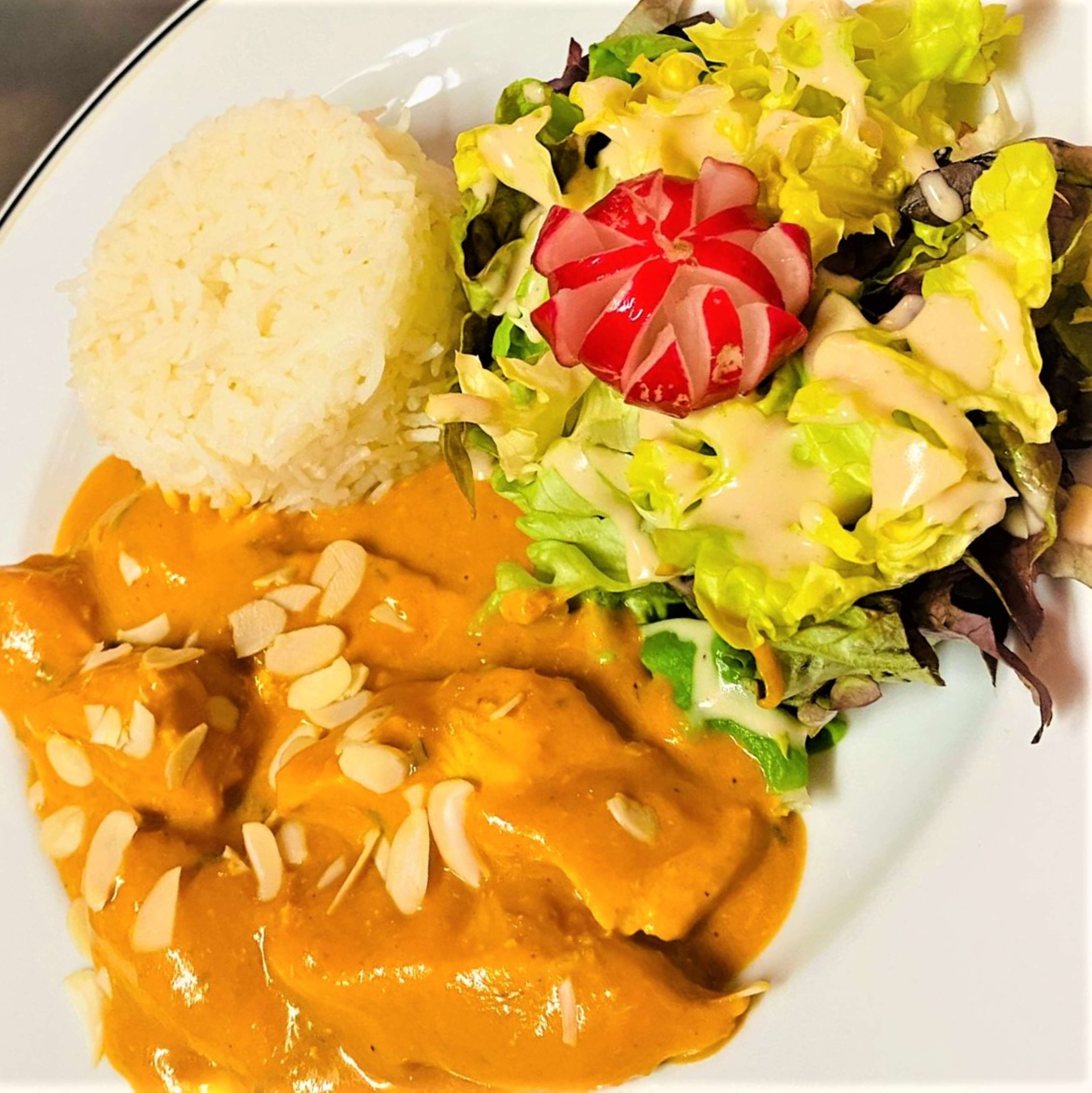 A plate with rice, a salad with radish, and a curry with almonds.