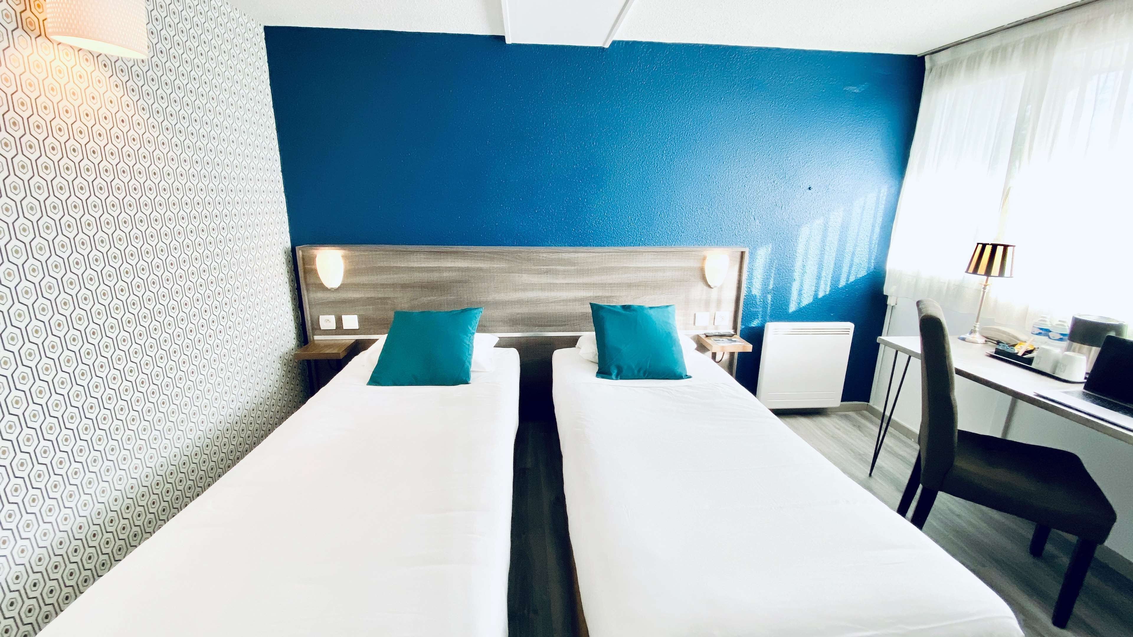 Habitación de hotel con dos camas, un escritorio, una silla, una lámpara y un radiador.
