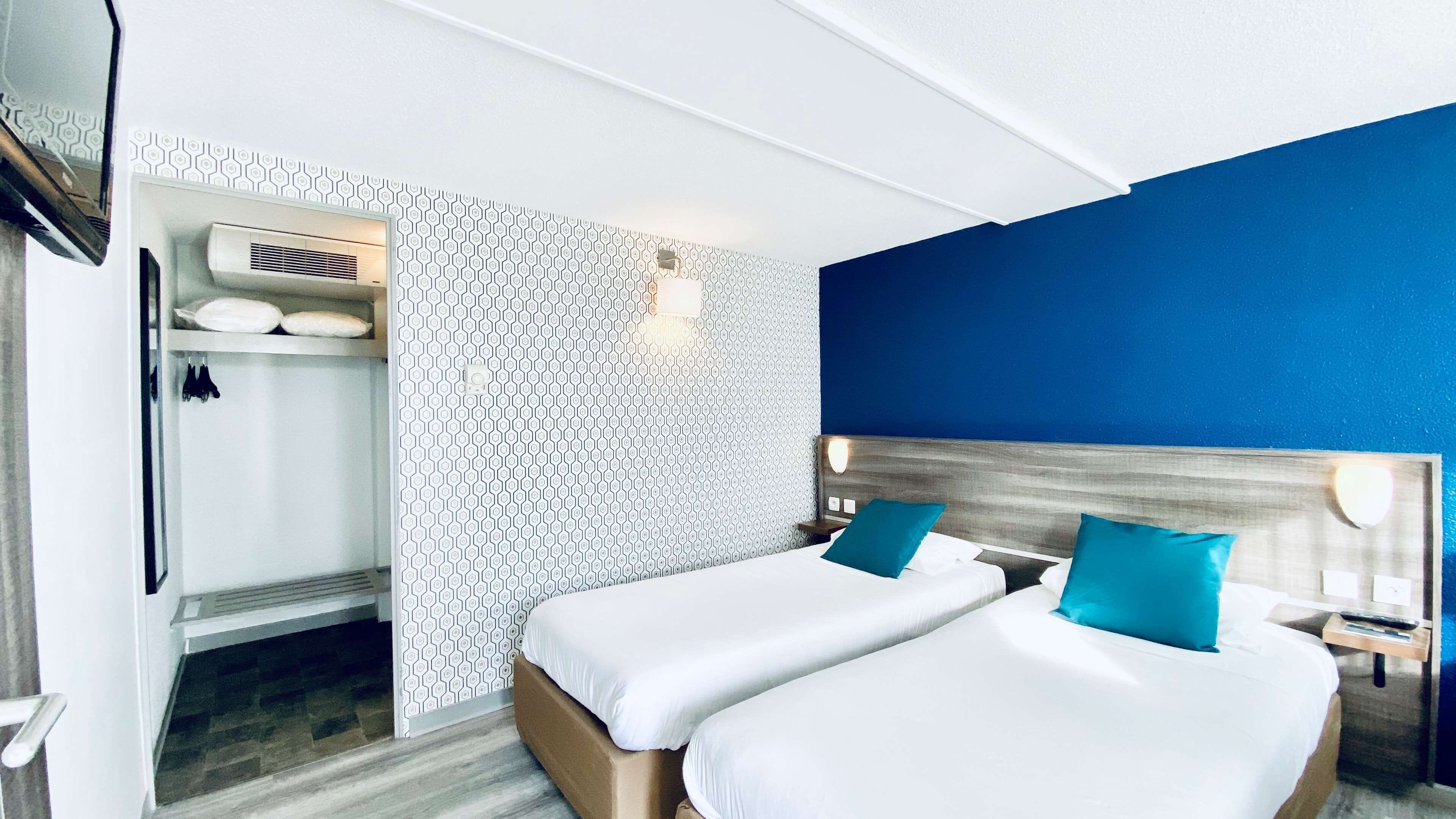 A hotel room with two beds, a wardrobe, a mirror, and a patterned wall.