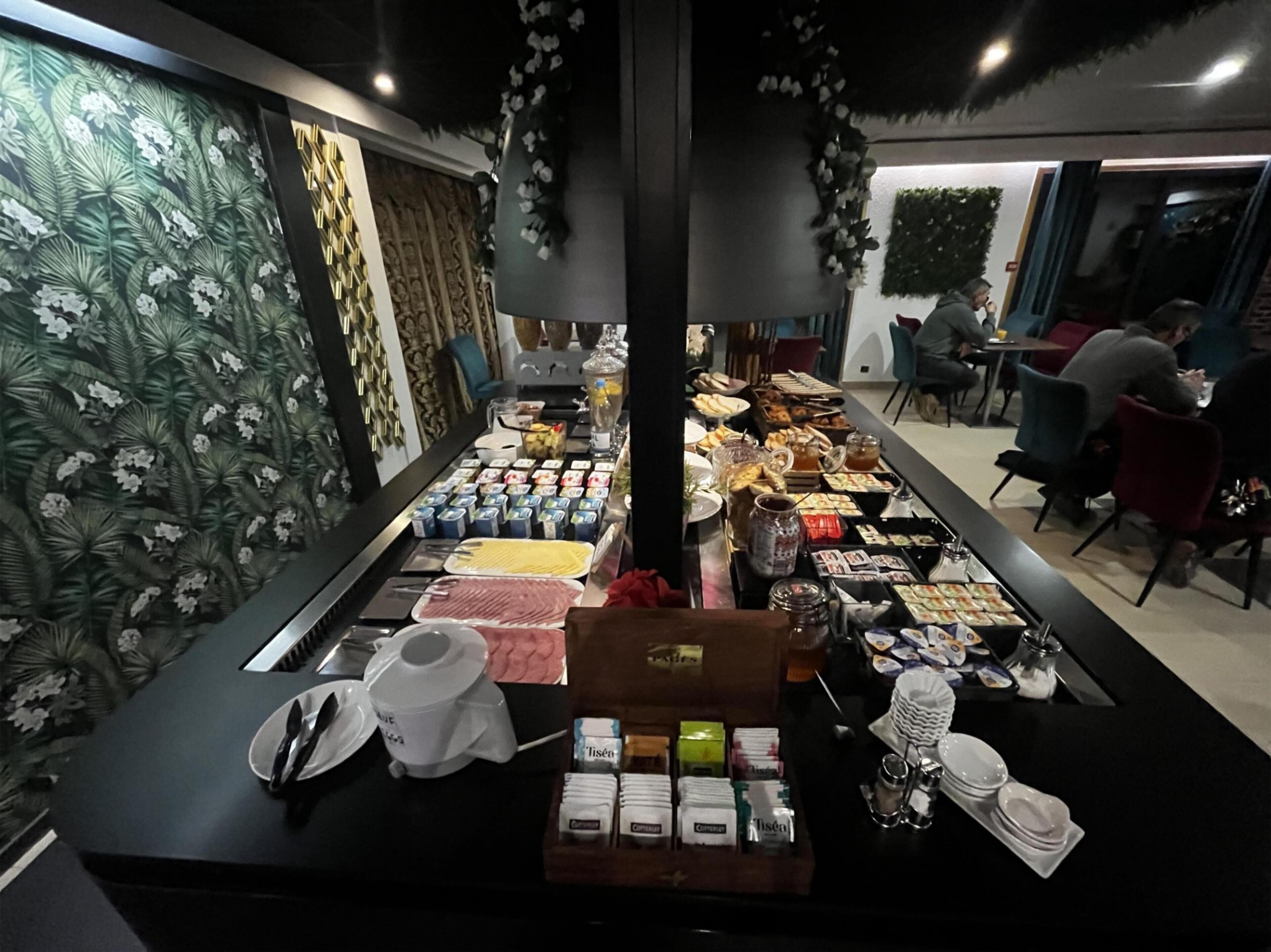 A buffet with various food items and condiments, a coffee machine, and a decorative wall with a floral pattern.