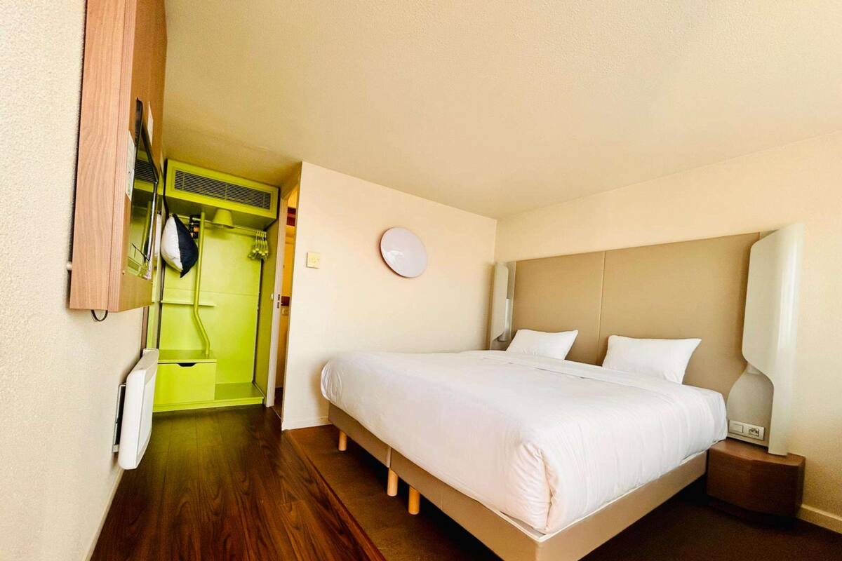 Een hotelkamer met een bed, nachtkastje, spiegel, kledingkast en een badkamer met douche.