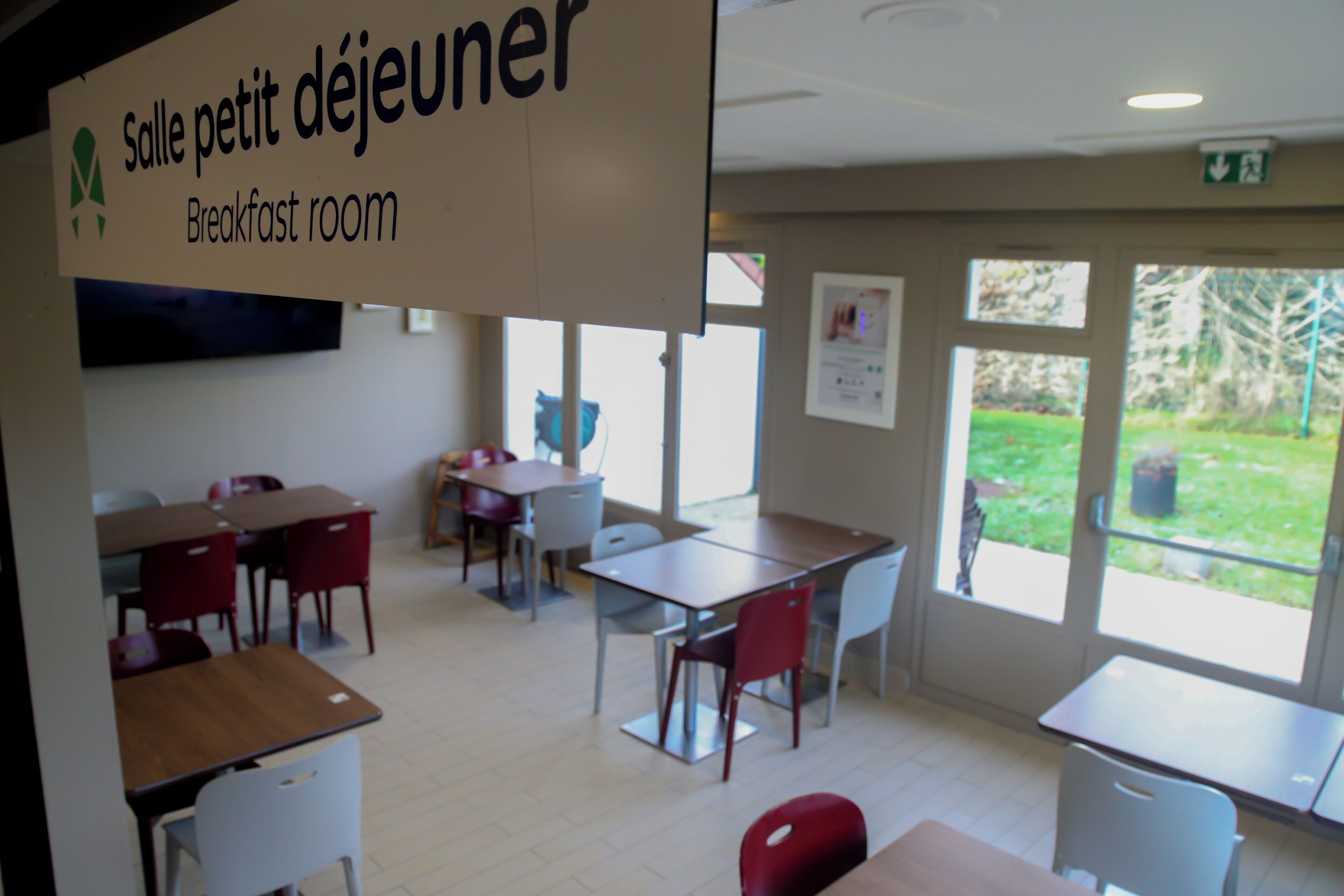 A breakfast room with tables and chairs, a sign indicating it's a breakfast area, and a view of the outdoors through the windows.