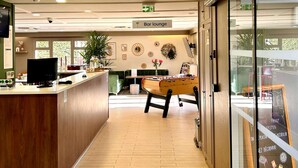 A bar lounge area with a foosball table, a bar counter, and a seating area with a view through a glass wall. - Hotel Campanile Montargis - Amilly (Amilly)