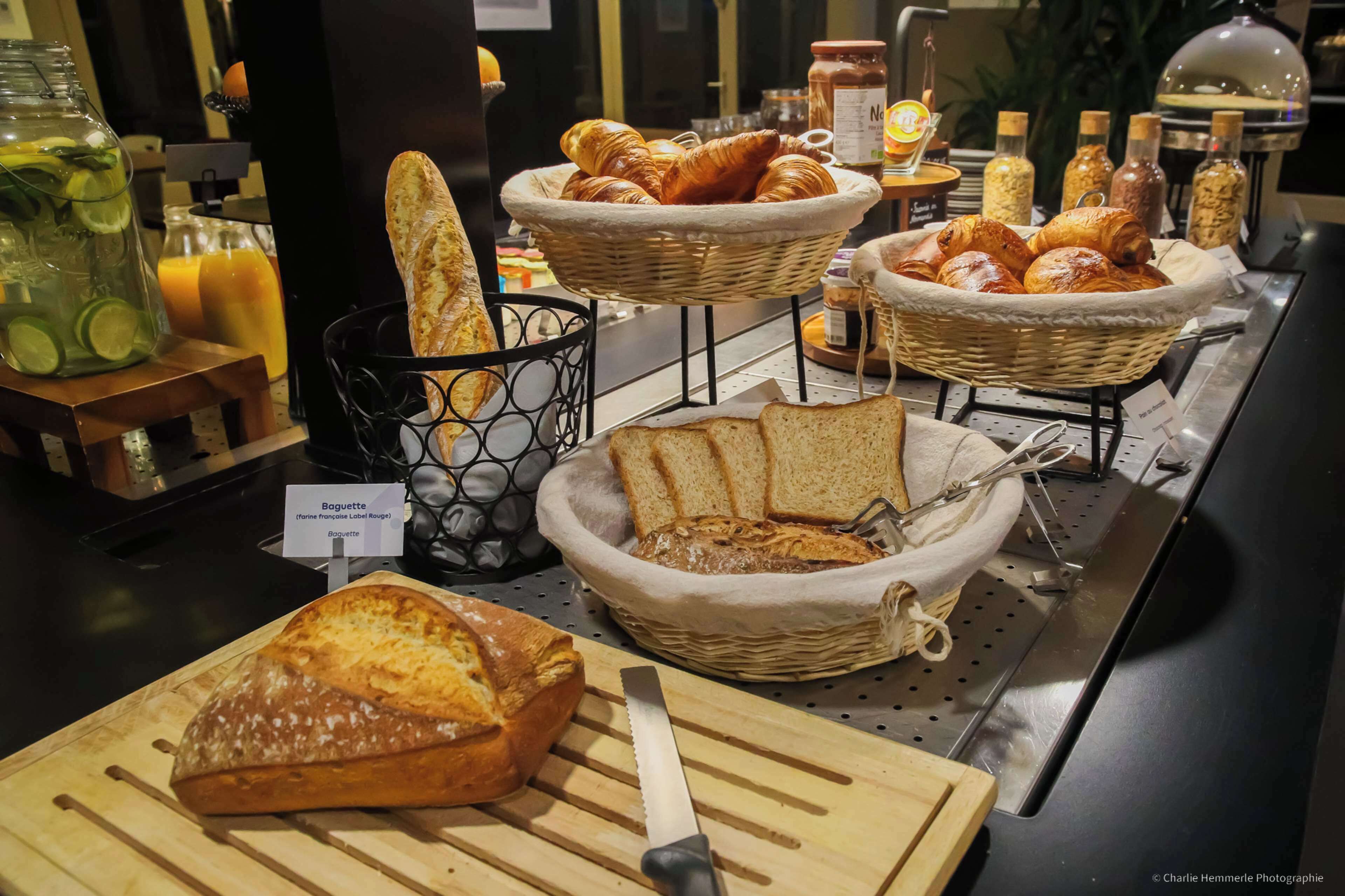 Um buffet de café da manhã com diversos pães, croissants e uma barra de pão em uma tábua de corte.