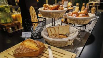 Um buffet de café da manhã com diversos pães, croissants e uma barra de pão em uma tábua de corte.