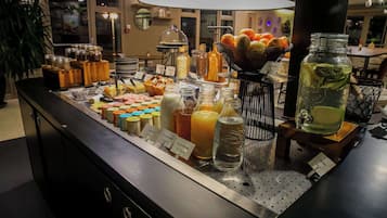 Un buffet proposant une variété de plats et de boissons, notamment des fruits, des fromages et des salades.