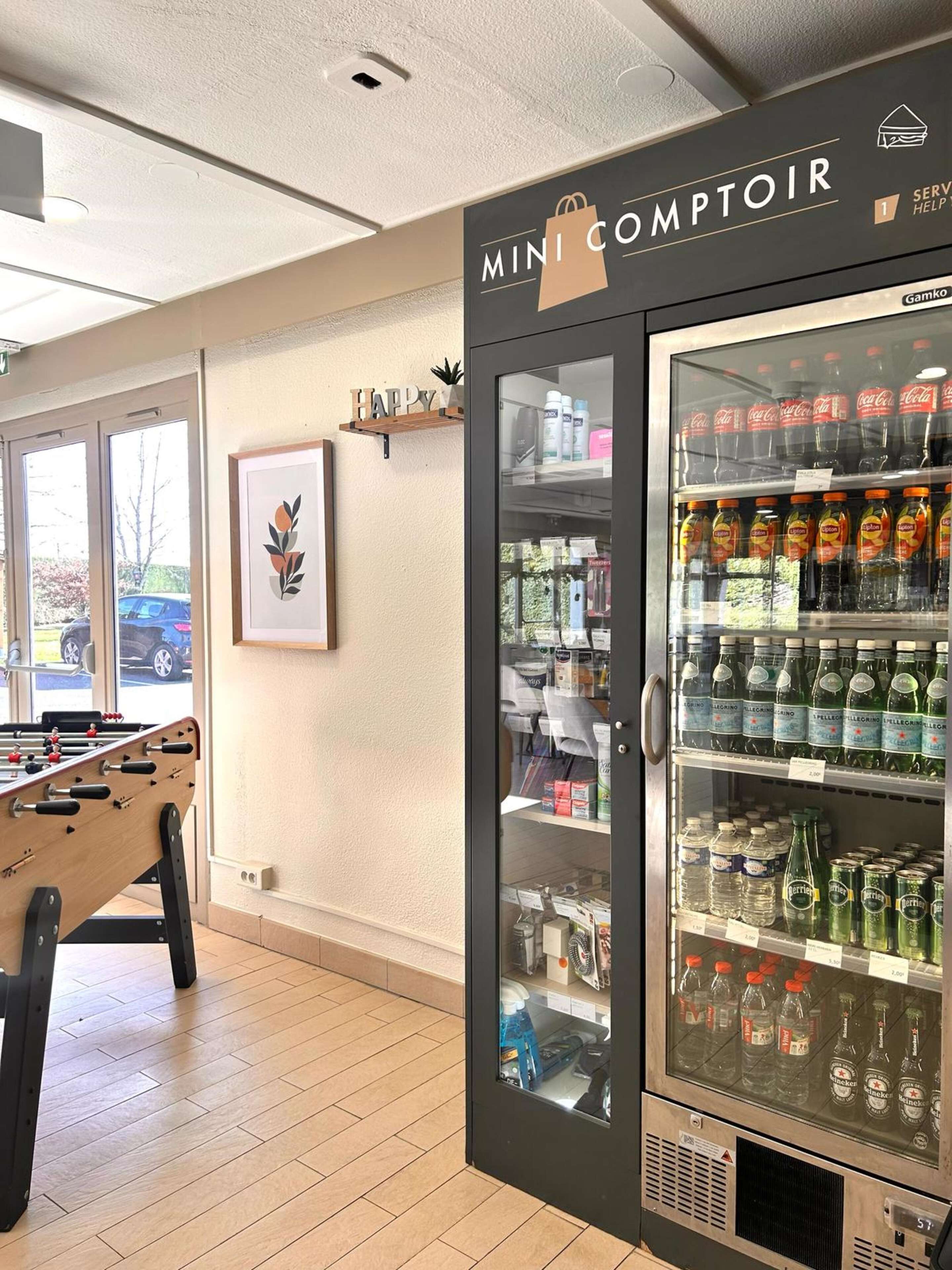 A mini kitchenette area with a fridge stocked with beverages, a foosball table, and a framed artwork on the wall.
