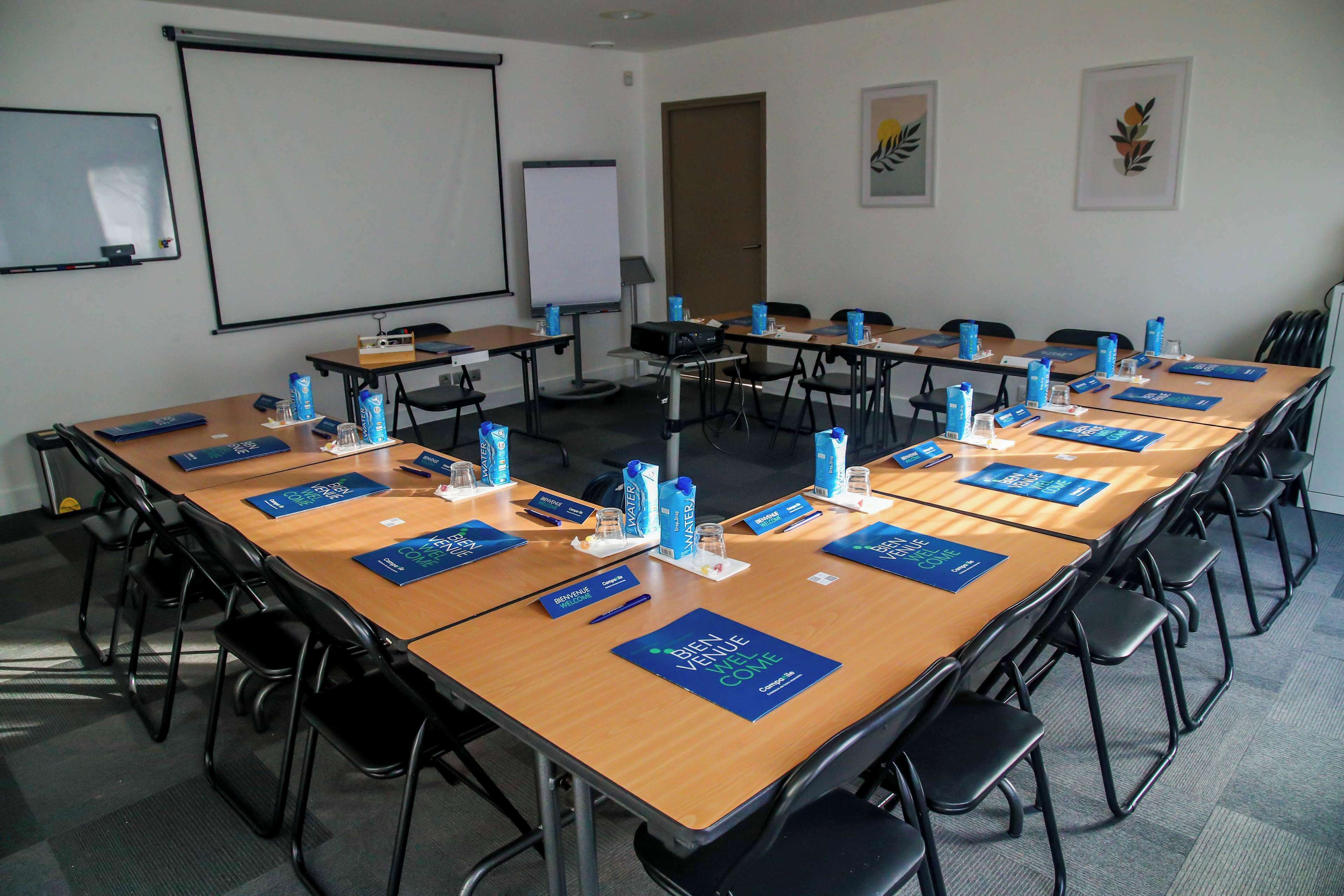 A conference room with long tables, chairs, and a projector screen.