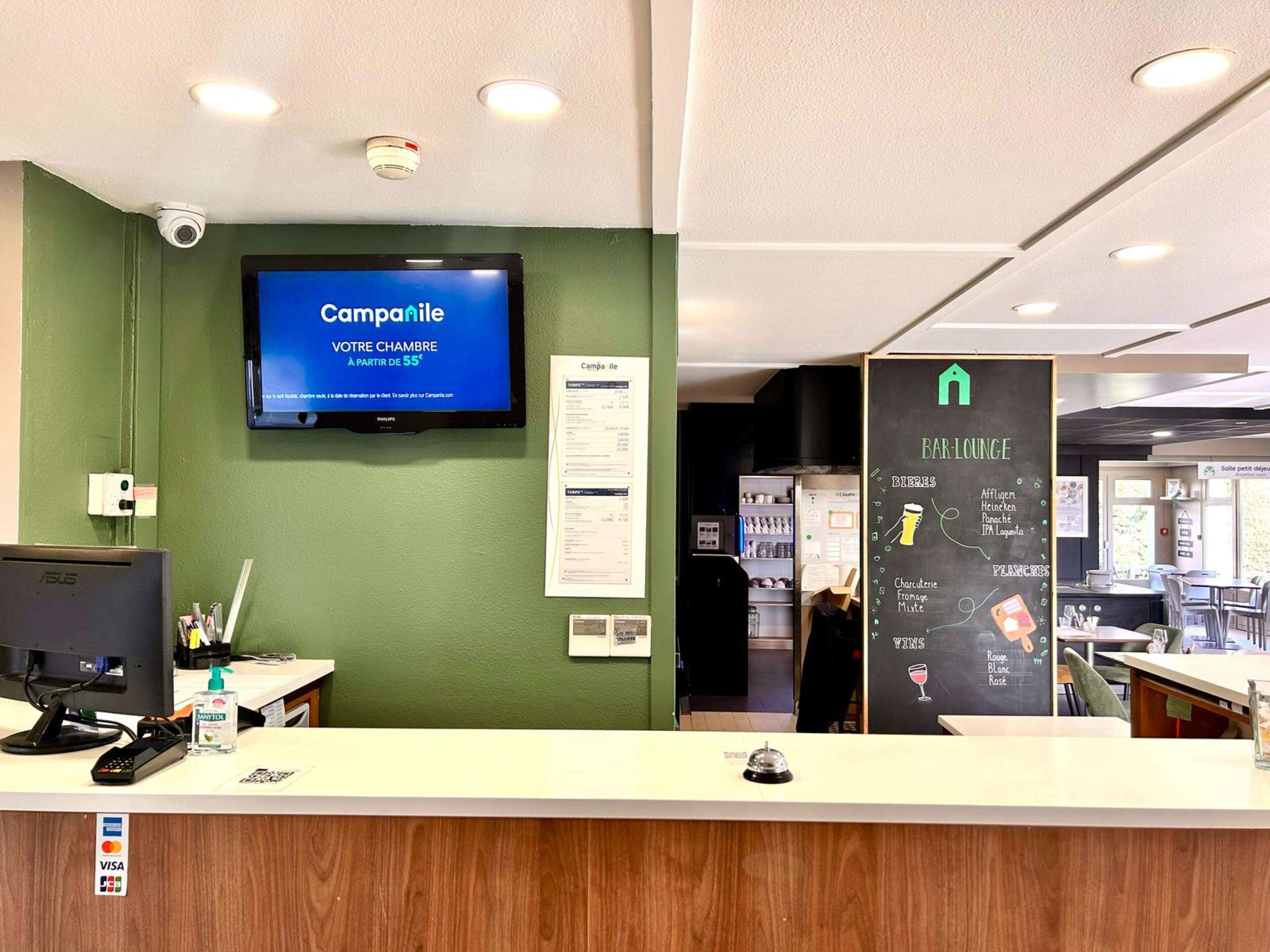 A reception area with a digital screen displaying 'Camparile' and a chalkboard menu for the bar lounge.
