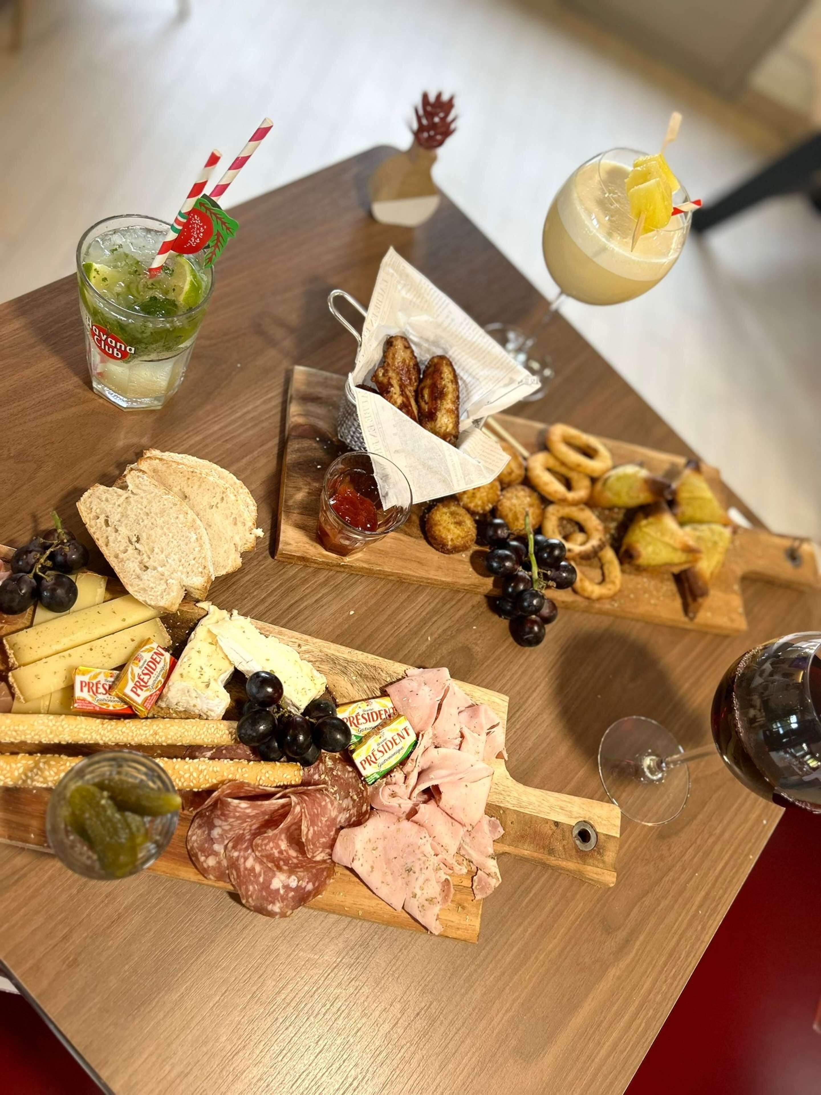 Ett träbord med olika sorters mat, inklusive ost, charkuterier, kex och en dryck med sugrör.