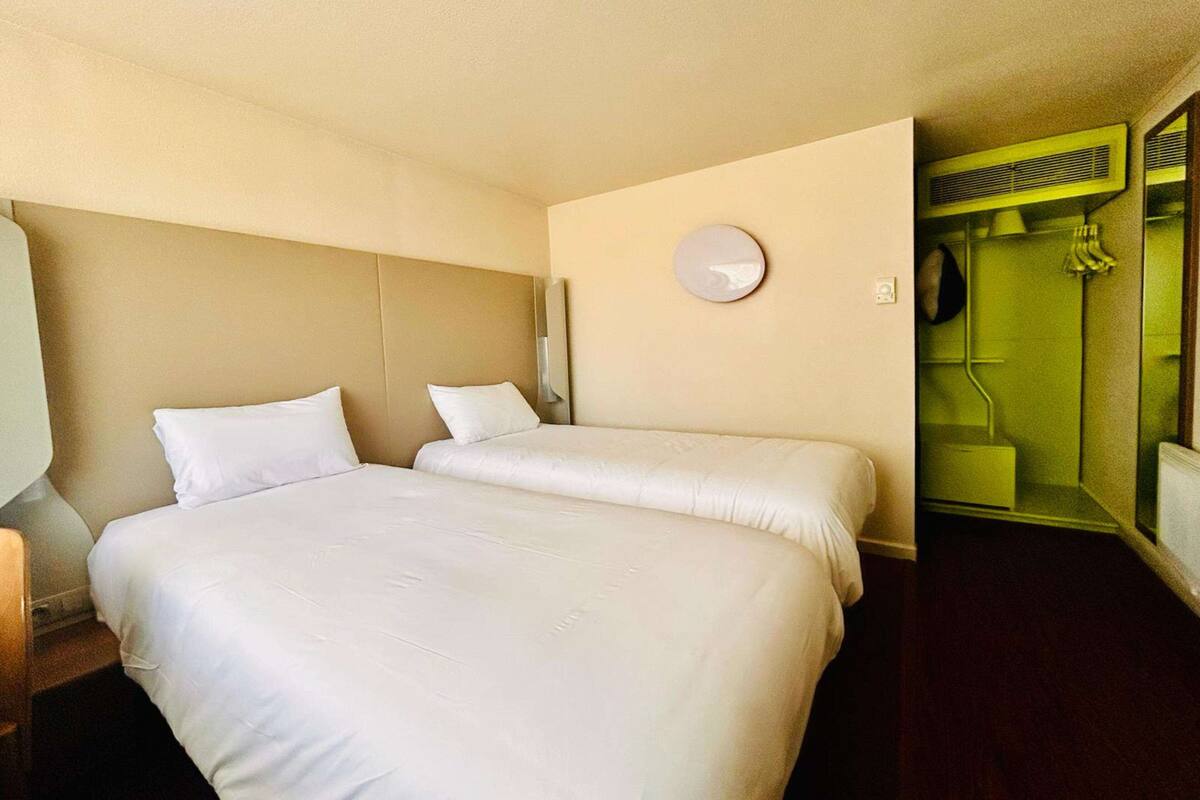 Een hotelkamer met twee bedden, een ronde wandklok, en een badkamer zichtbaar door een geopende deur.