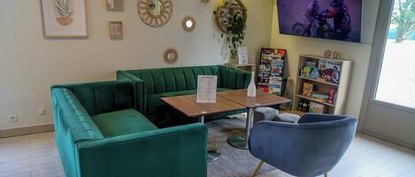 A green sofa, a blue chair, a wooden table, and a TV screen in a room with a tiled floor and a bookshelf.