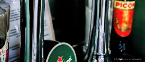 Una llave de bar con etiqueta de Heineken, una botella de Picon y varios vasos.
