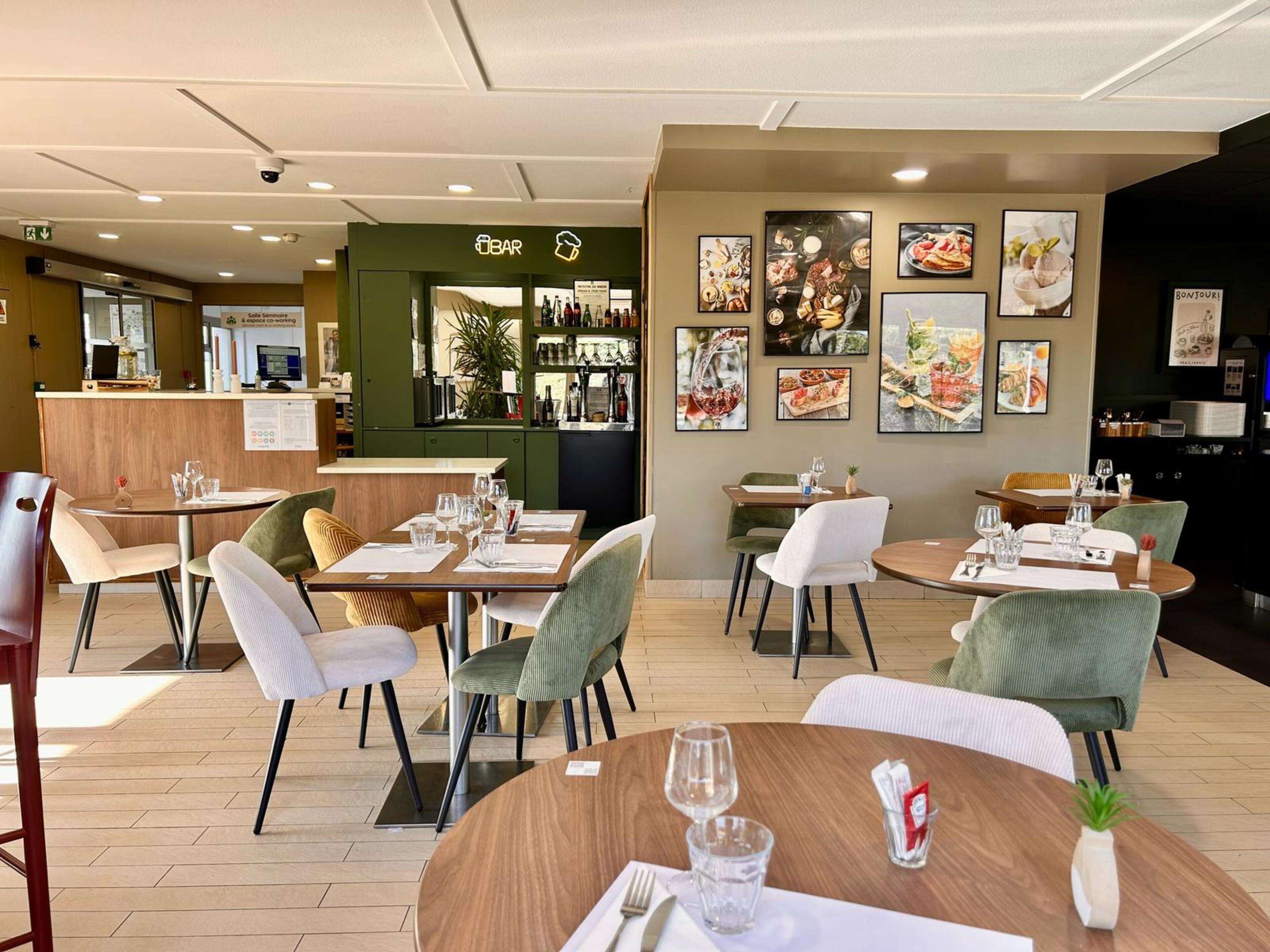 Een modern restaurantinterieur met ronde tafels, groene beklede stoelen en een bar met een groene toonbank.