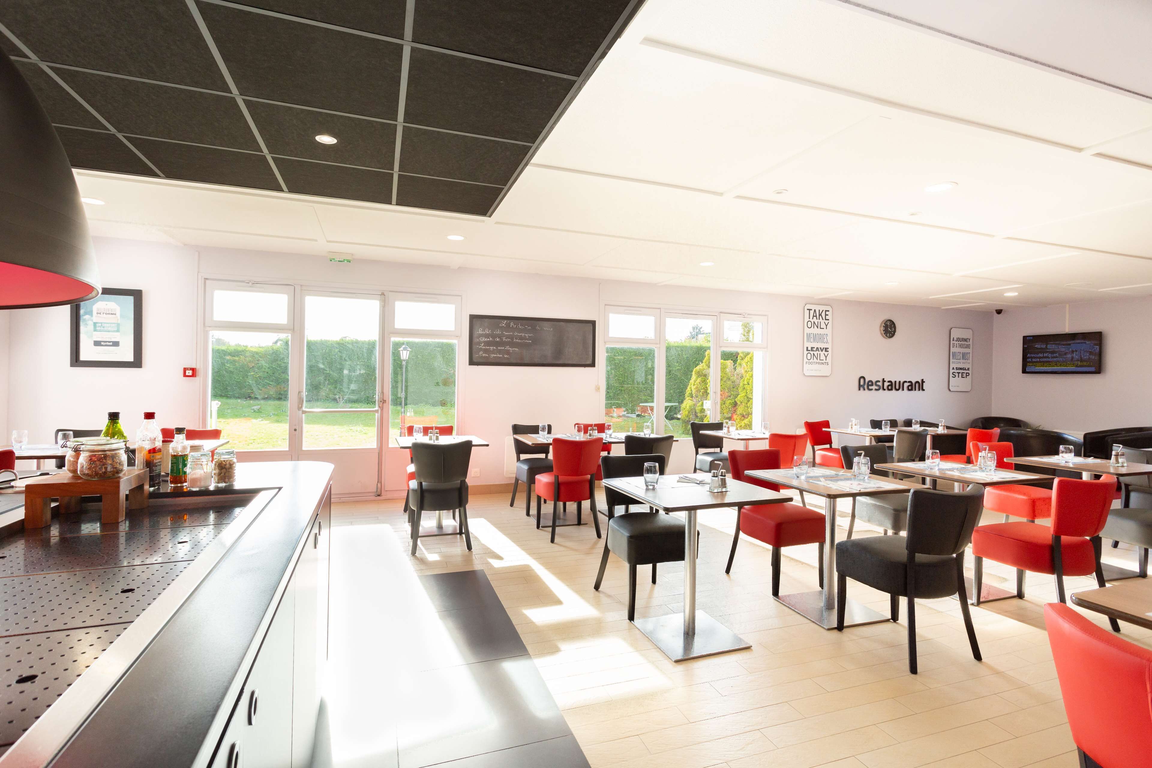 A modern restaurant with a long counter, multiple tables, and red chairs.