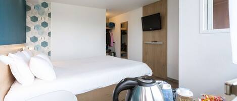 A hotel room with a bed, a kettle, a tray with snacks, a TV, and a geometric wall design.