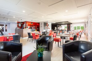 A modern restaurant with red and black chairs, a central bar area, and a view of the outdoors.