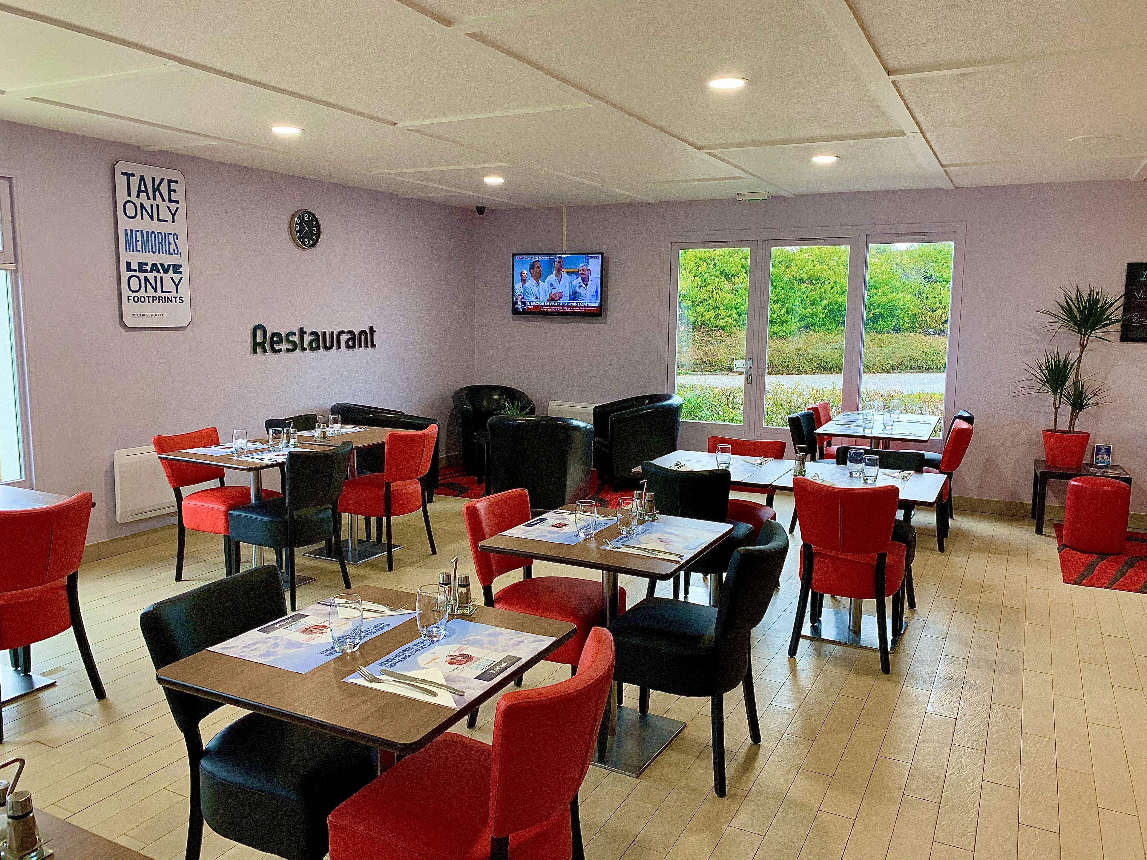 A restaurant with tables and chairs, a television screen, and a sign on the wall.