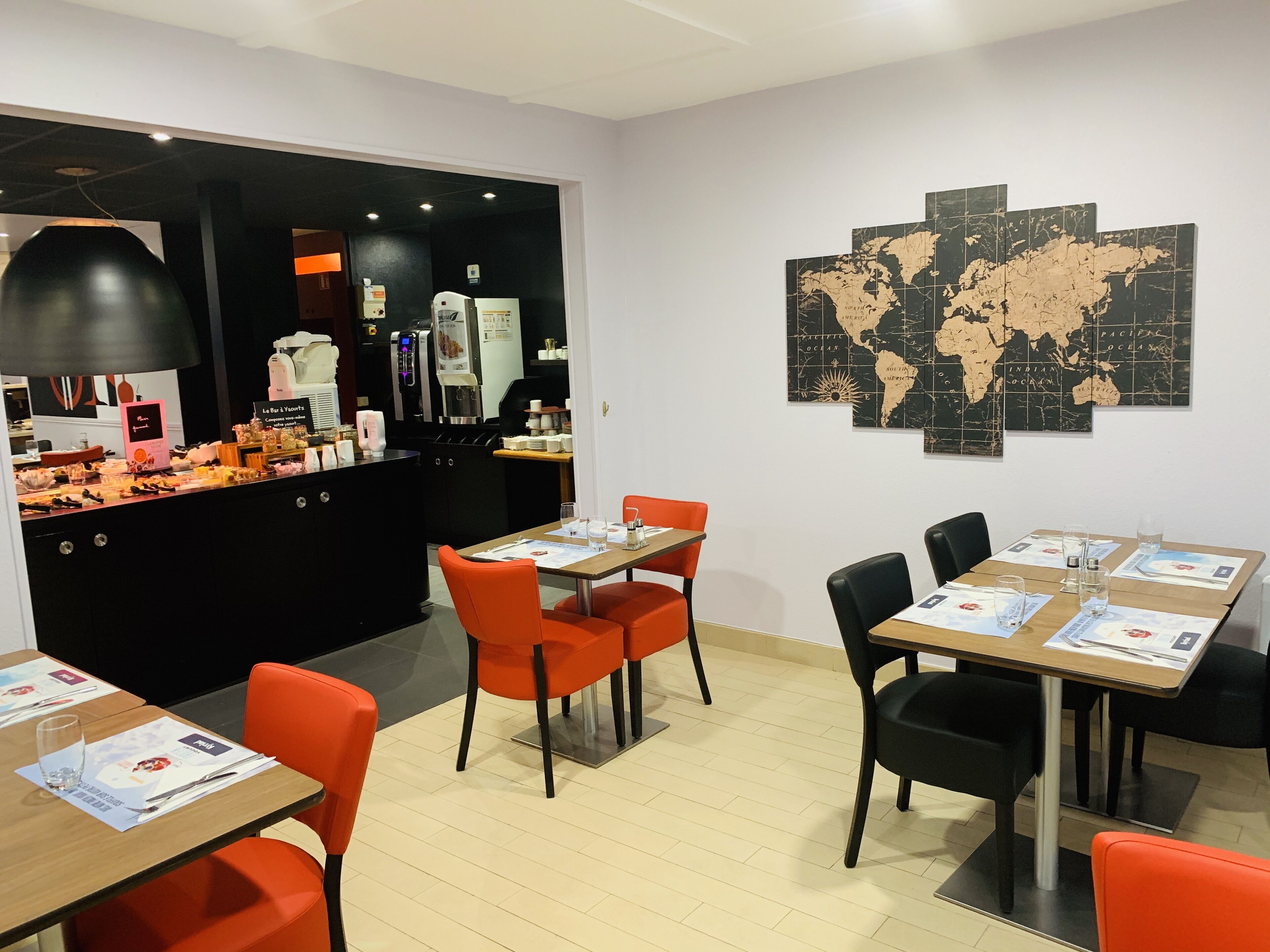 Un restaurant avec un comptoir où sont exposés les plats proposés, une machine à café, des tables avec des menus et une carte du monde accrochée au mur.