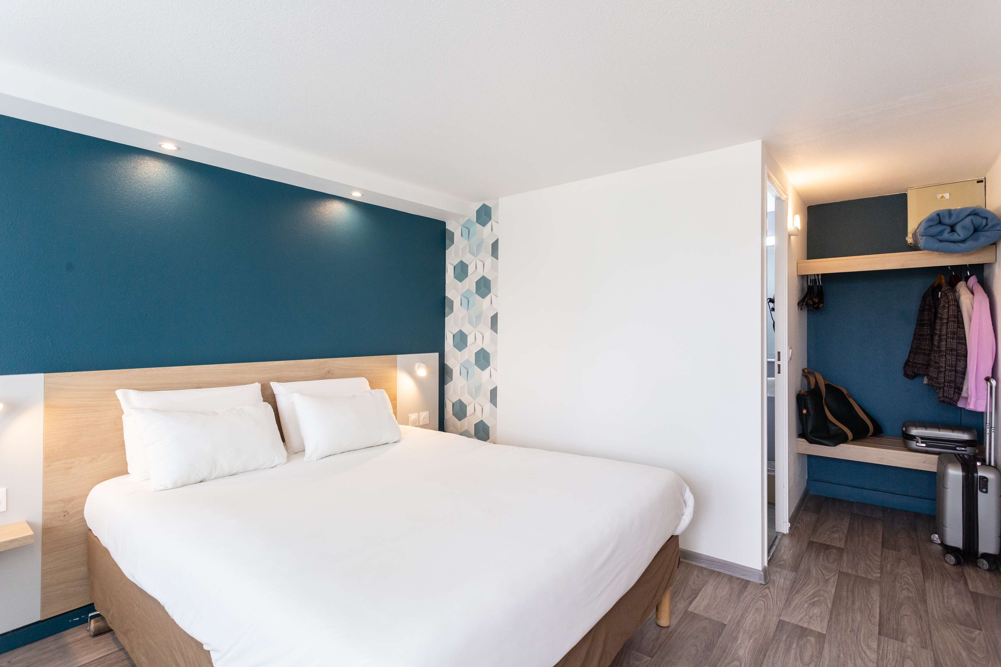 Una habitación de hotel moderna con una cama grande, un armario y un banco con equipaje.