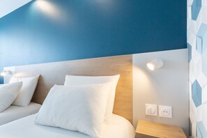 A modern hotel room with a wooden headboard, white bedding, and a geometric-patterned wall.