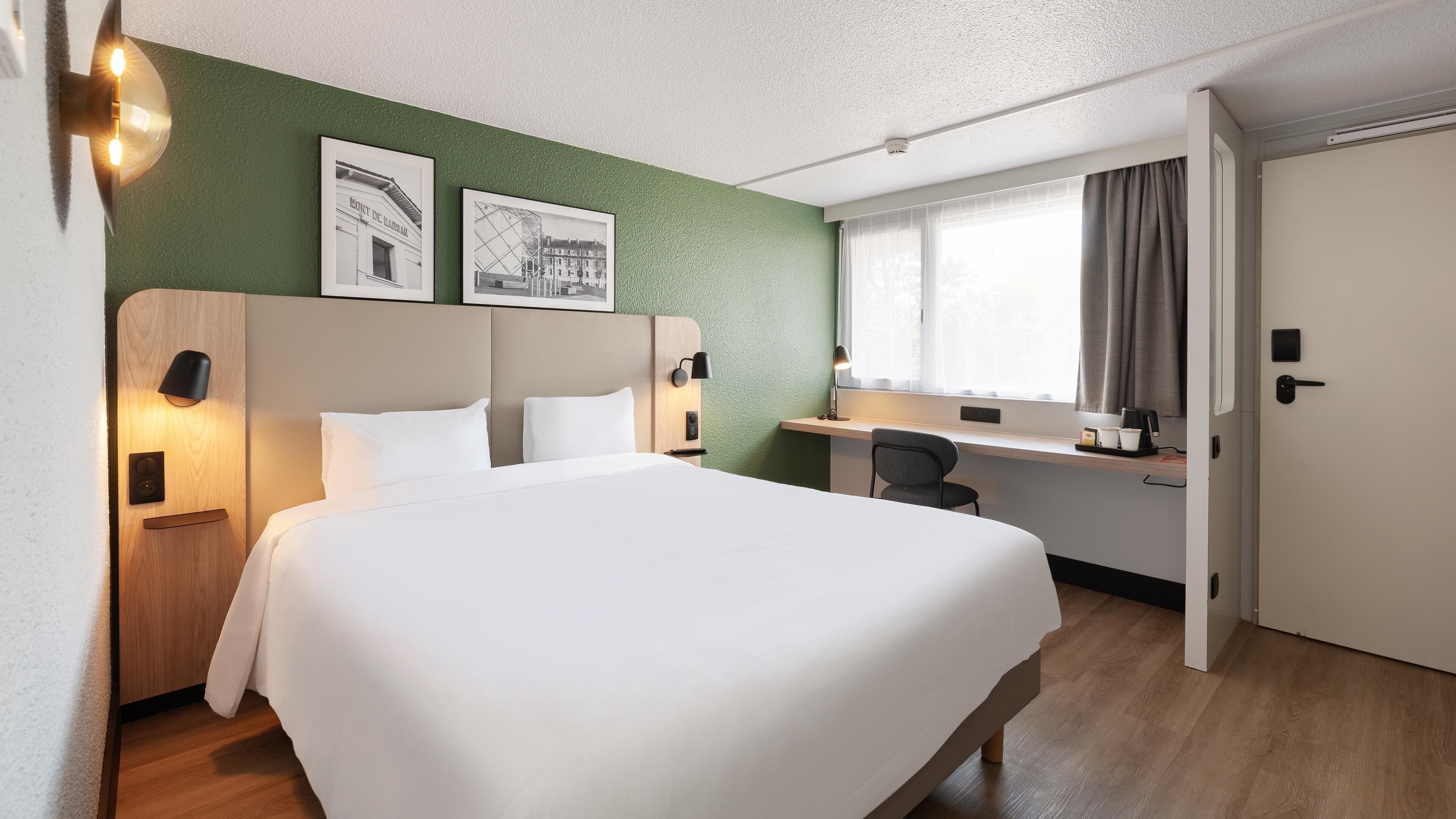 A hotel room with a large bed, a desk, a chair, and a window with curtains.