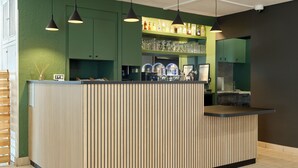A bar area with a counter, shelves with bottles, glasses, and a menu board. - Campanile NATURE - Epône (Epone)