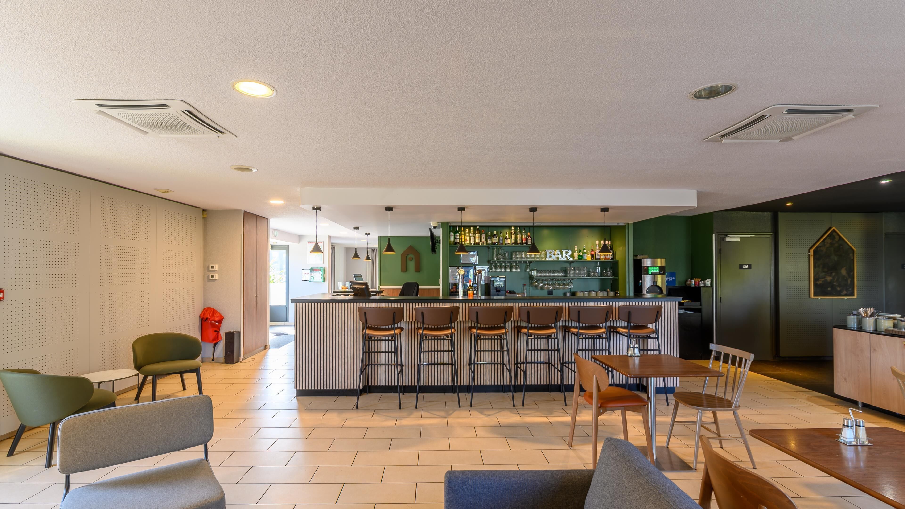 Eine moderne Bar mit einer Theke, Barhocker und einer Sitzgelegenheit mit Tischen und Stühlen.