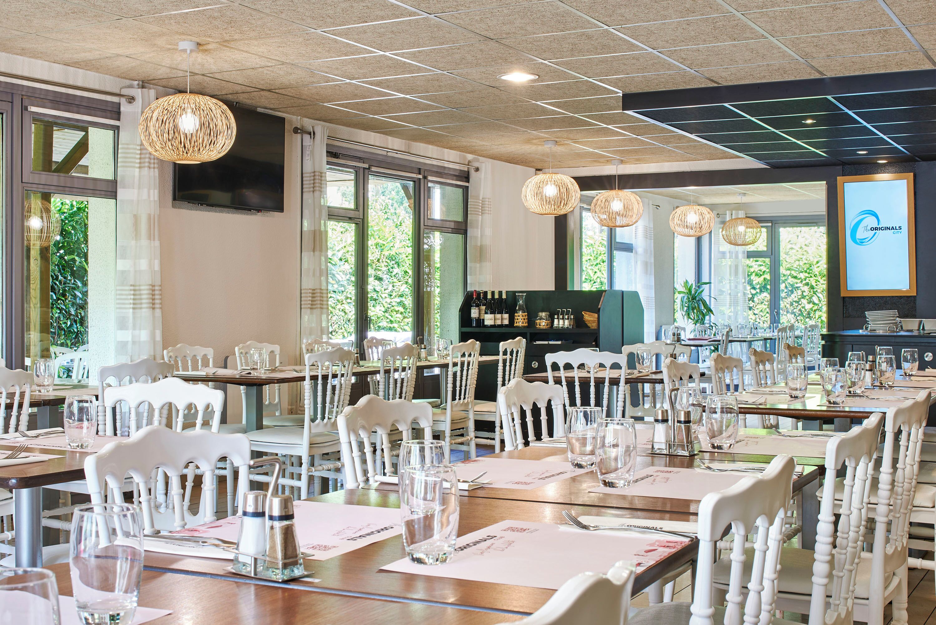 A dining area with white chairs, wooden tables, and hanging wicker chandeliers.